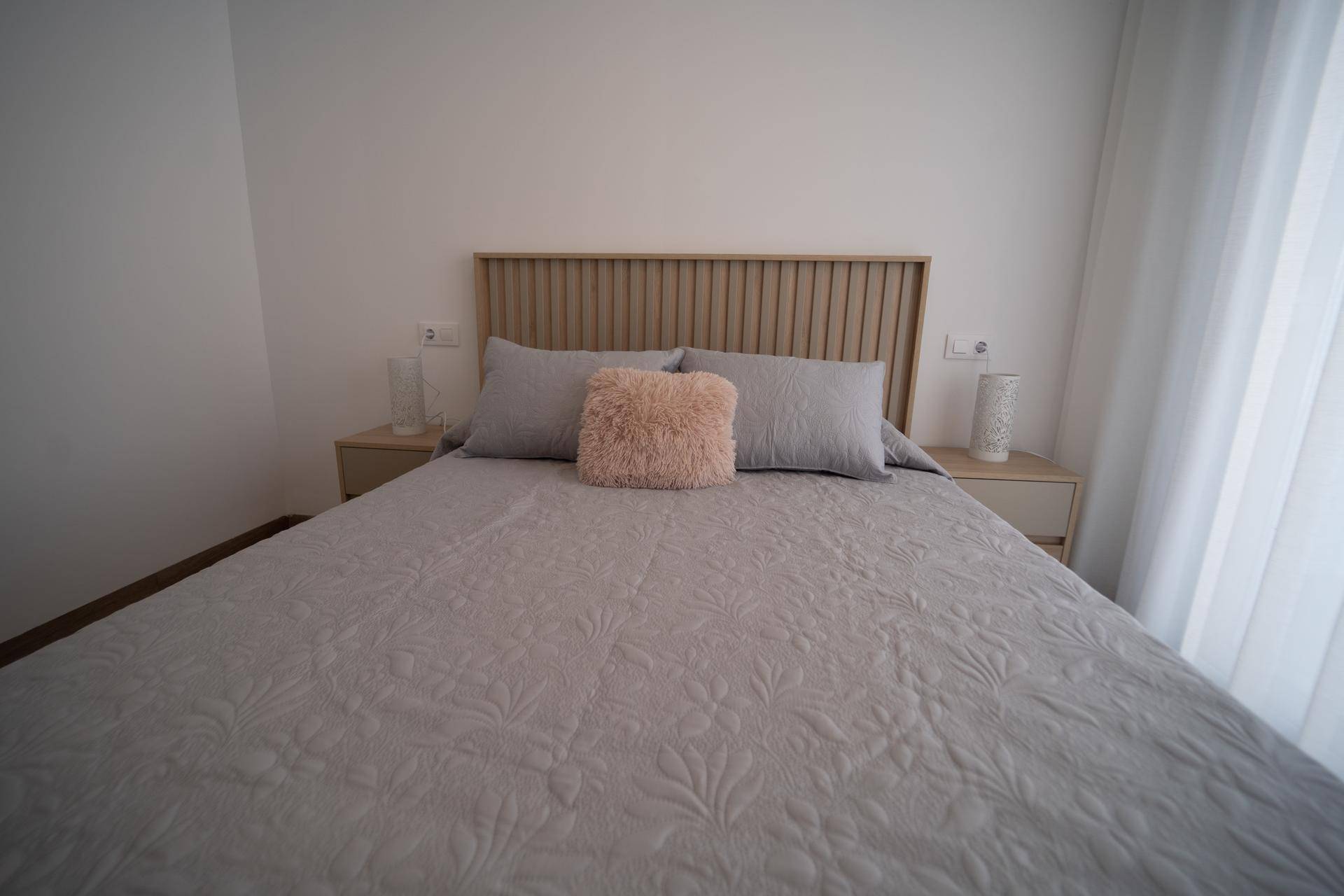 Helles Schlafzimmer mit Doppelbett, Holzkopfteil und modernem Laminatboden.