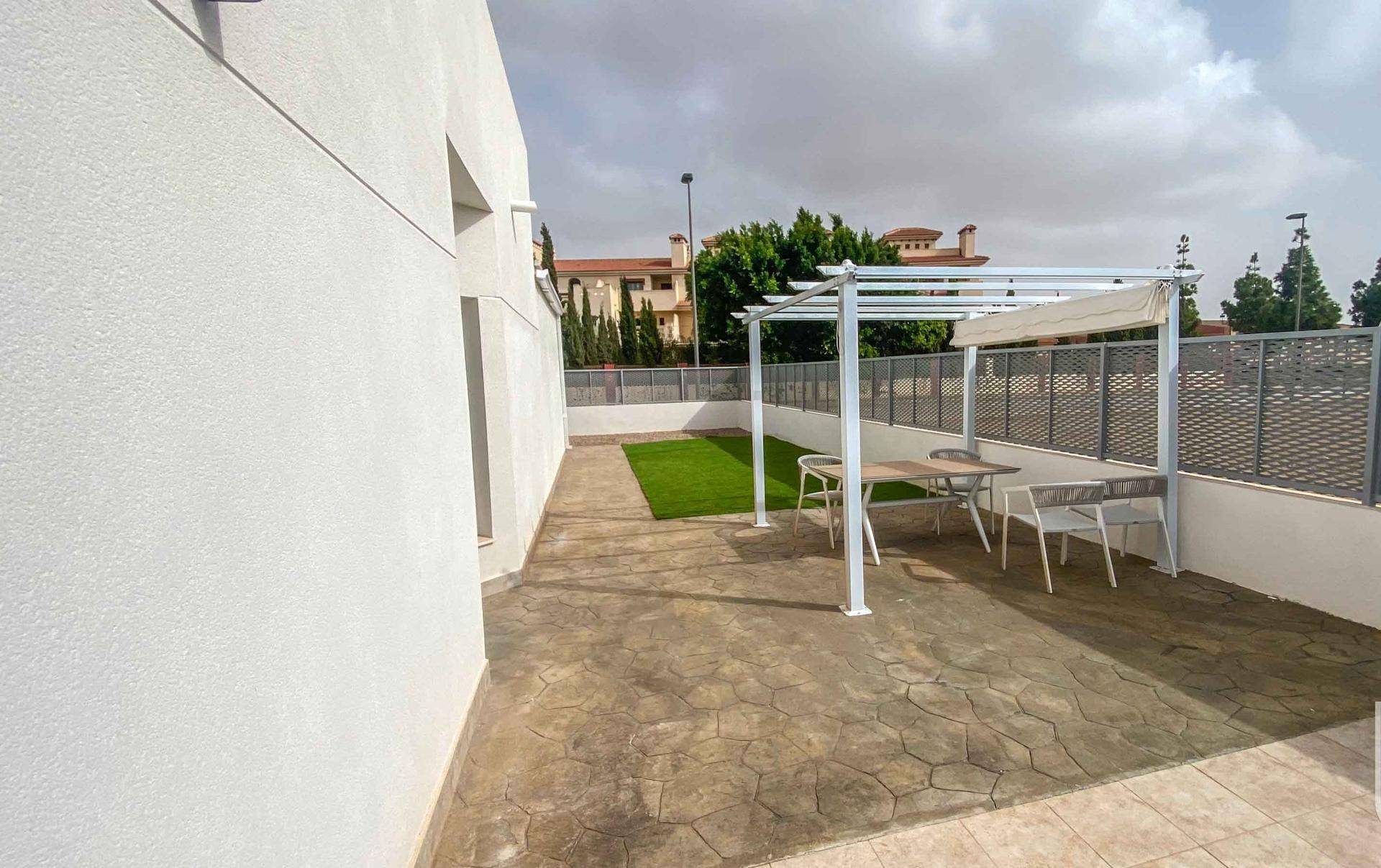 Gepflasterte Terrasse mit Pergola, Esstisch und kleinem Rasenbereich.