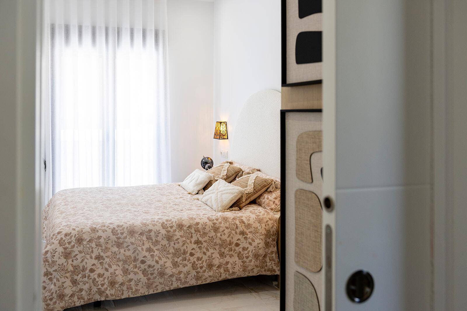 Detailansicht des Schlafzimmers mit Doppelbett, Nachttisch und hellem Vorhang.