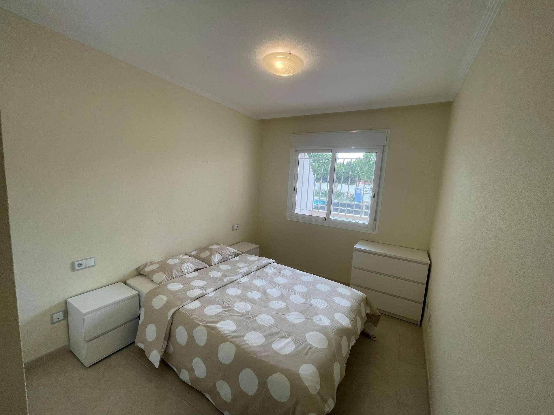 Helles Schlafzimmer mit Doppelbett, Nachttischen und Kommode, ausgestattet mit Fliesenboden.