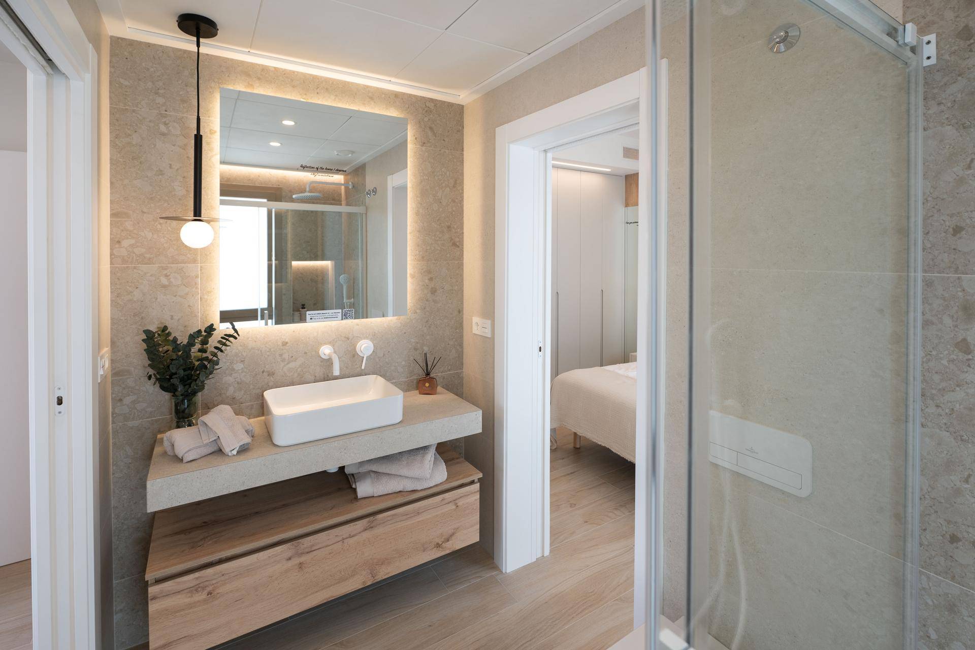Modernes Badezimmer mit Einzelwaschbecken, beleuchtetem Spiegel und Zugang zum Schlafzimmer.