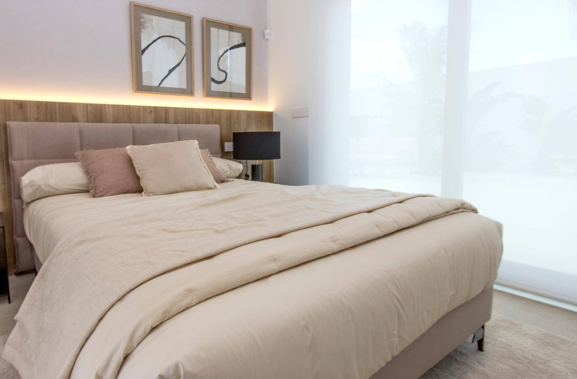 Helles Schlafzimmer mit beigem Bett, Holzakzenten und großen Fenstern.