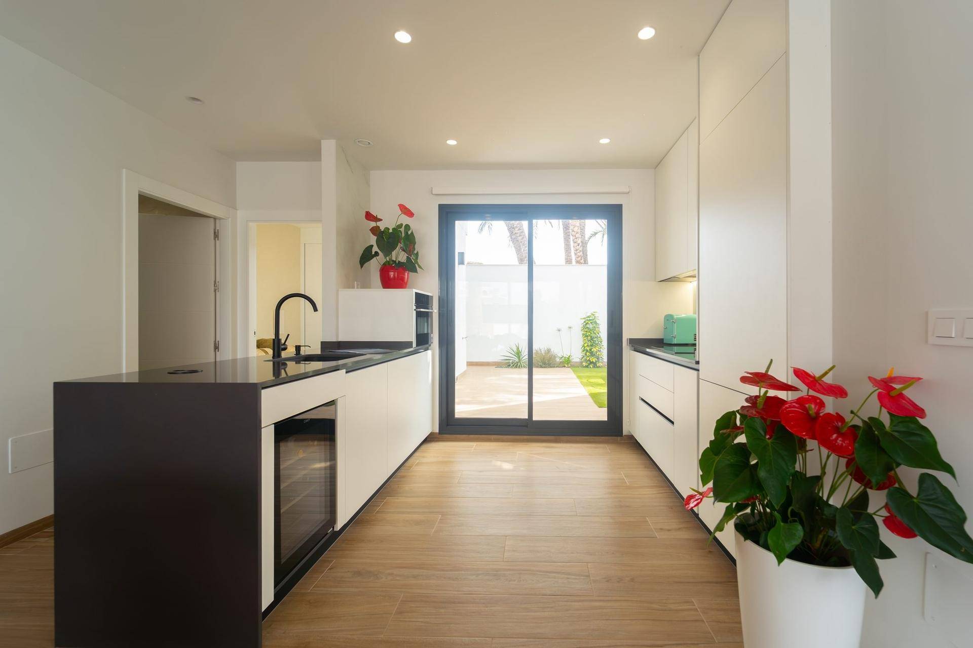 Moderne Küche mit weißen Schränken, dunkler Arbeitsplatte und direktem Zugang zum Garten.