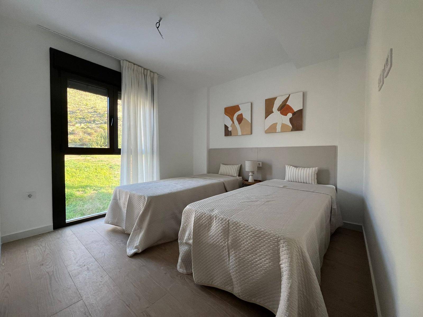 Helles Schlafzimmer mit zwei Einzelbetten, Holzboden und Blick ins Grüne.