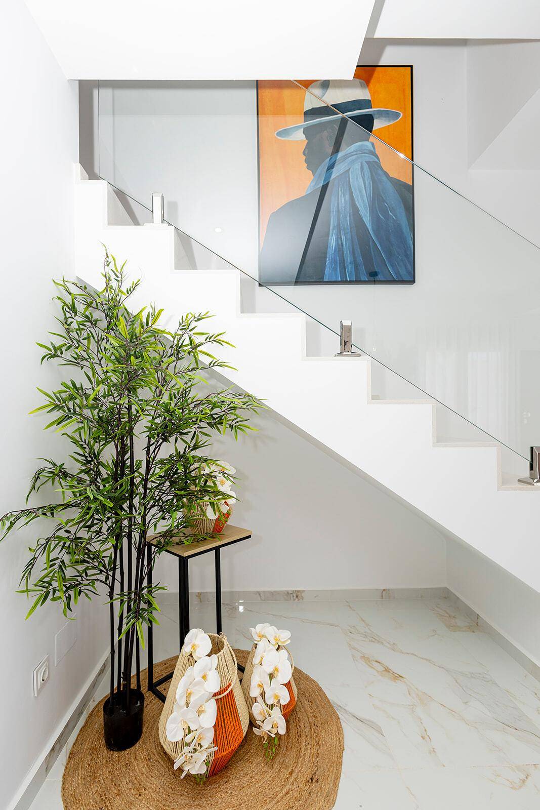 Heller Eingangsbereich mit moderner Treppe, Glasgeländer und dekorativen Pflanzen.