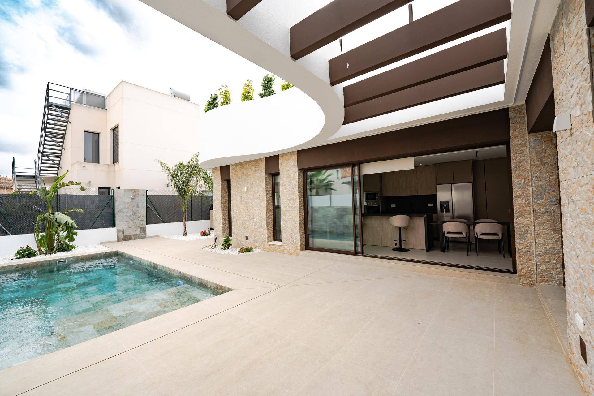 Außenbereich mit Pool und Blick auf die moderne Küche durch große Glasschiebetüren, ideal für Unterhaltung.