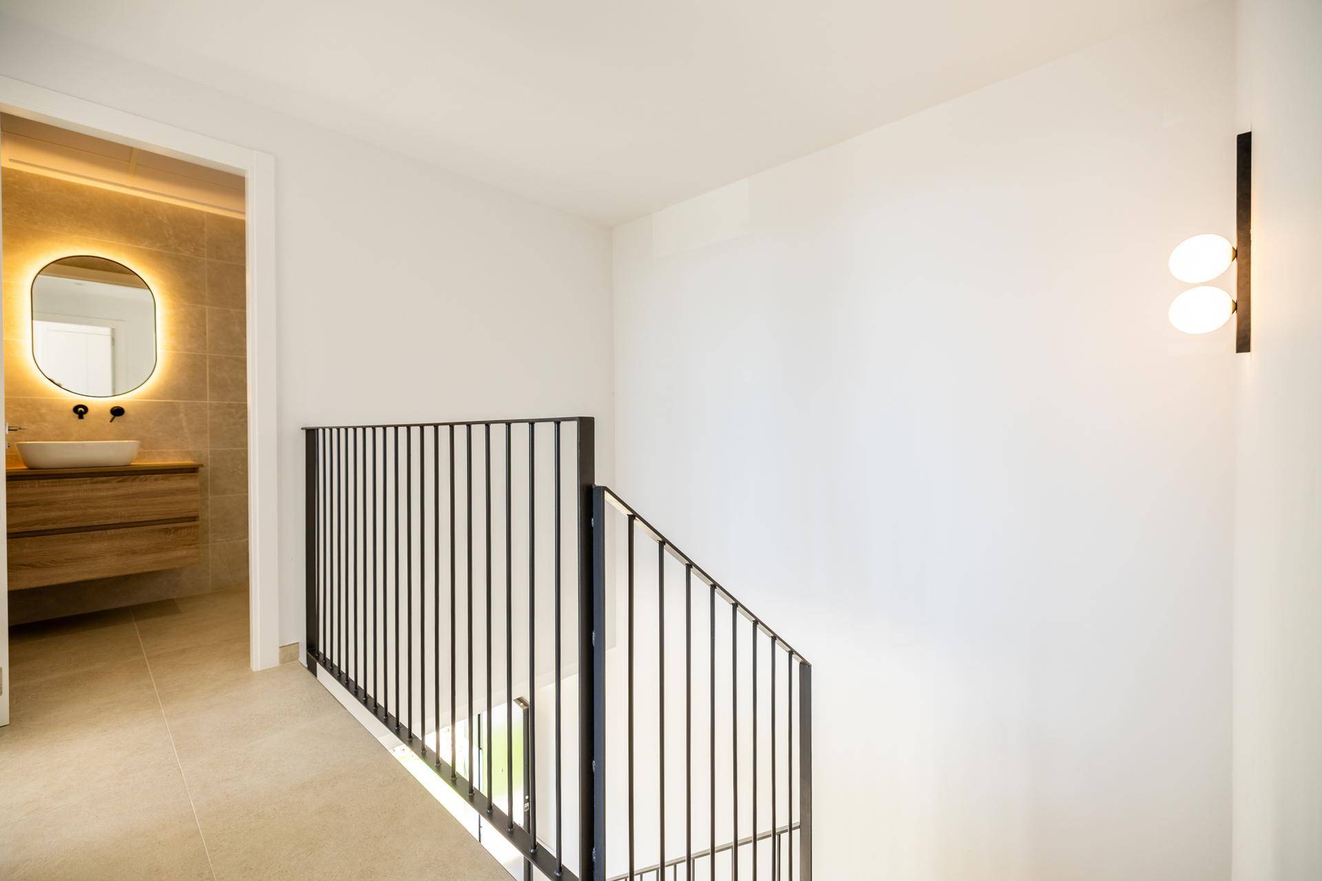 Heller Flur mit moderner Treppe und Blick in ein stilvolles Badezimmer mit beleuchtetem Spiegel.