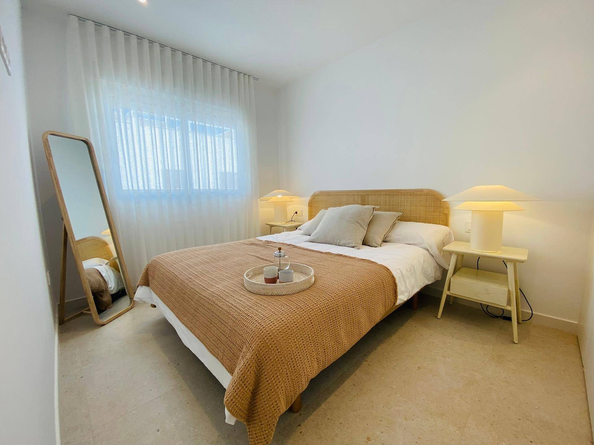 Helles Schlafzimmer mit Doppelbett, großem Spiegel und Nachttischen mit Lampen.