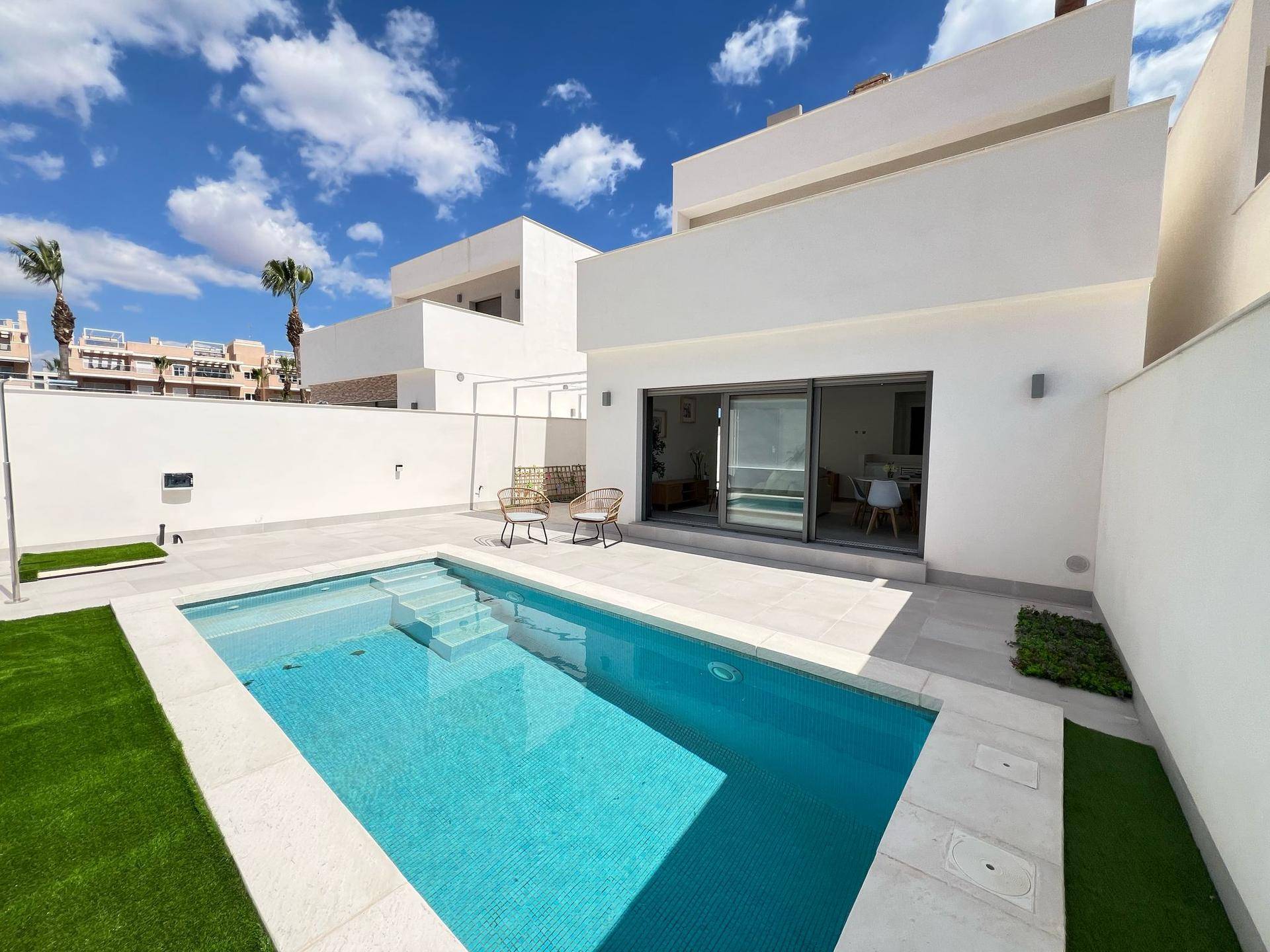 Moderne Villa mit privatem Pool, Sonnenterrasse und kleinem Gartenbereich unter blauem Himmel.