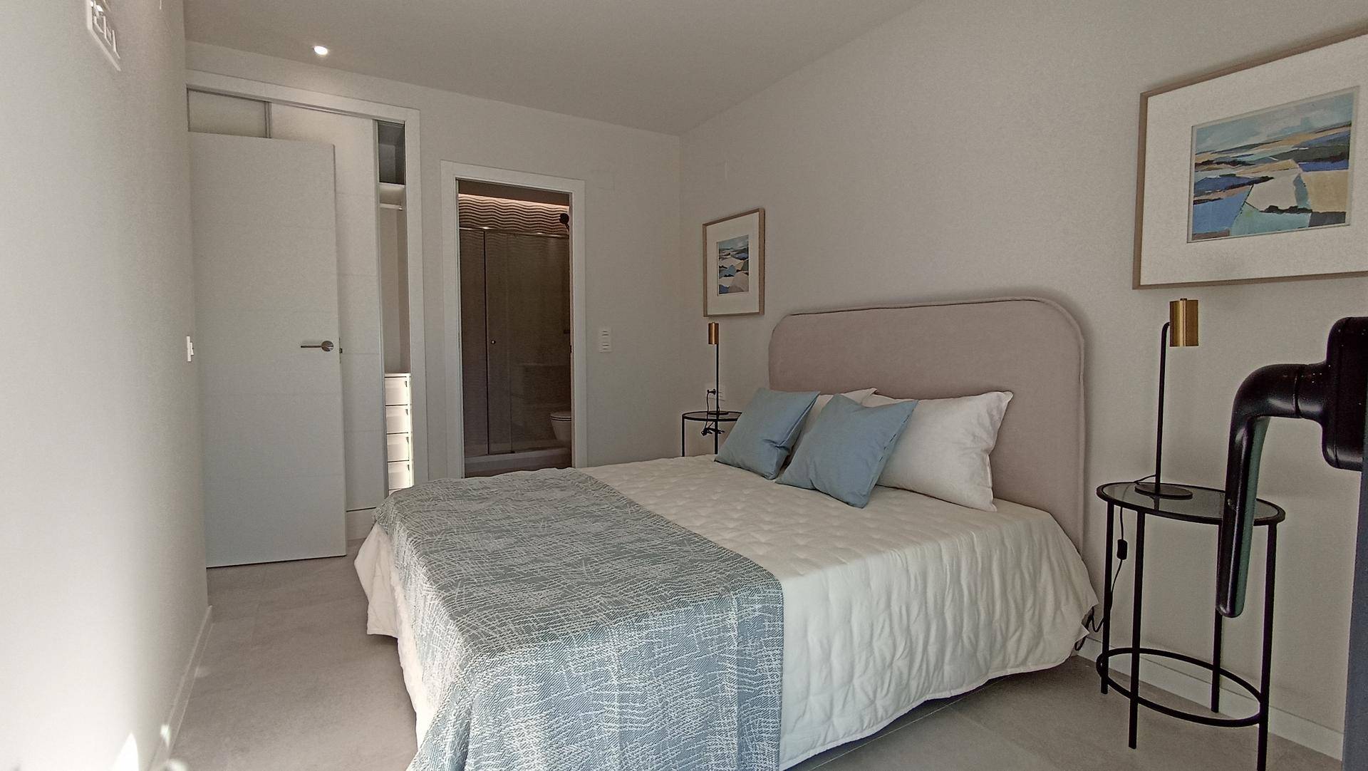 Helles Schlafzimmer mit Doppelbett, minimalistischer Einrichtung und Zugang zum Badezimmer.