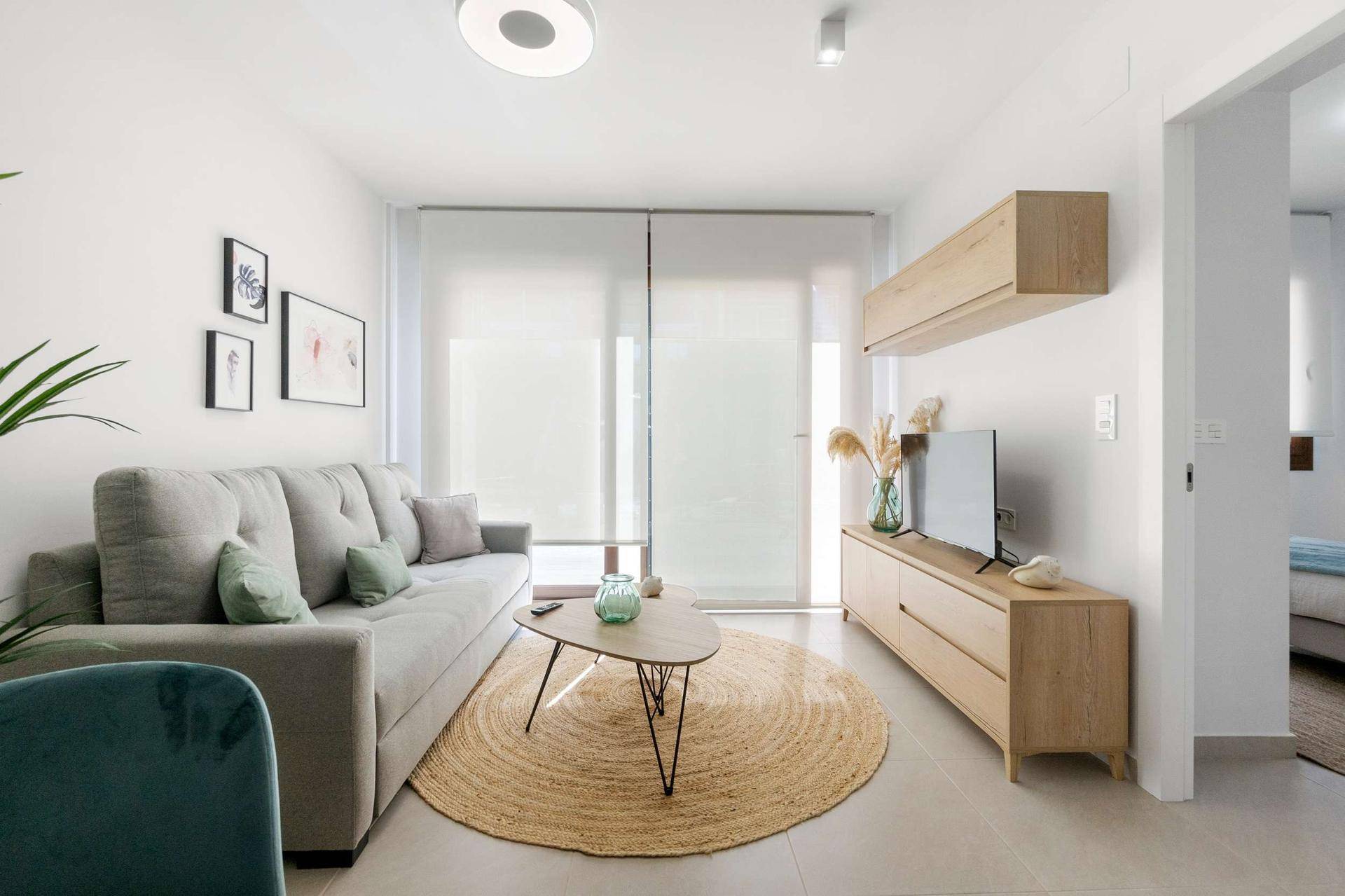 Modern eingerichtetes Wohnzimmer mit hellem Sofa, Teppich und großen Fenstern mit Rollos.