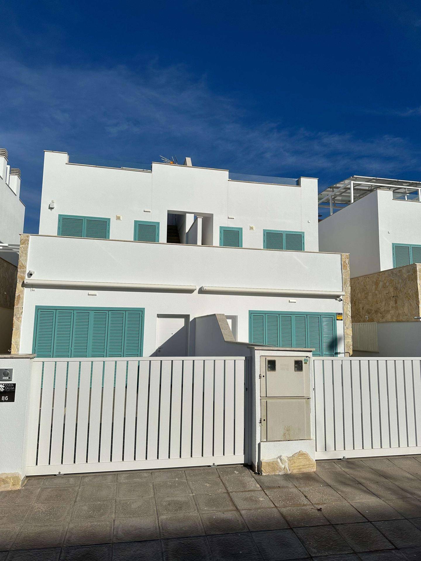 Moderne weiße Fassade eines Reihenhauses mit türkisfarbenen Fensterläden und Eingangstor.