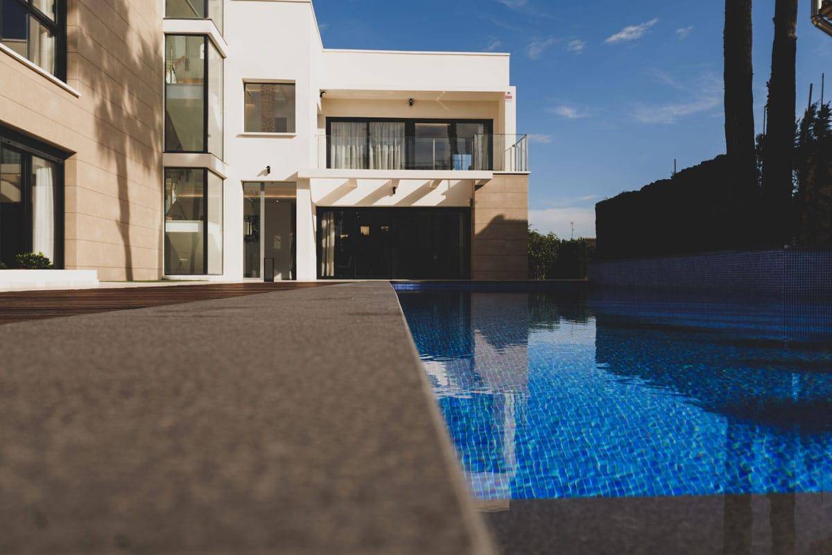 Nahaufnahme des glitzernden Pools mit blauen Mosaikfliesen und der modernen Villa im Hintergrund.