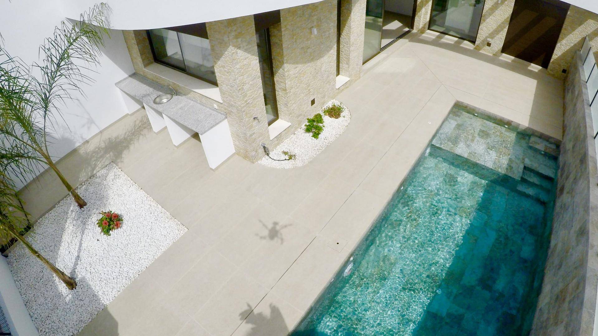 Vogelperspektive auf den Innenhof der modernen Villa mit Pool und Außenküche, umgeben von weißem Kies.