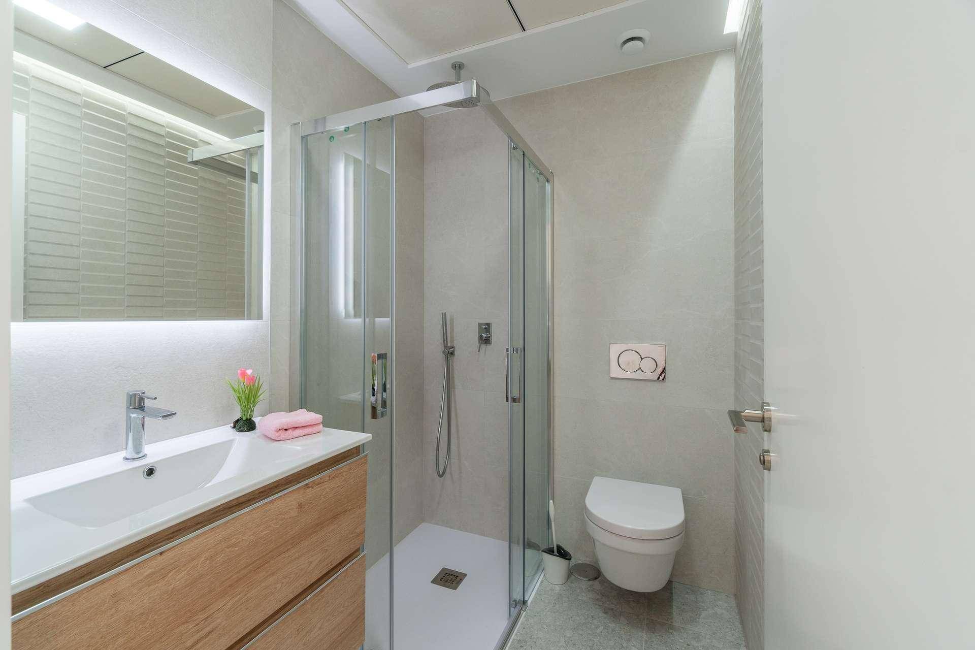 Modernes Badezimmer mit Duschkabine, wandhängendem WC und elegantem Waschtisch mit Spiegel.