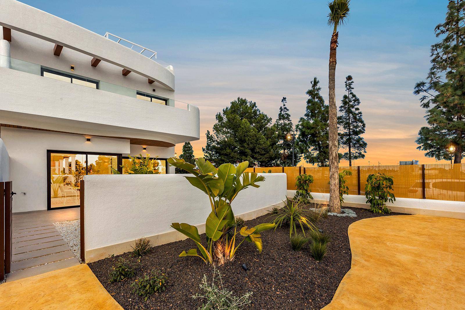 Gartenbereich mit mediterranen Pflanzen und der modernen Architektur des Gebäudes in der Abenddämmerung.