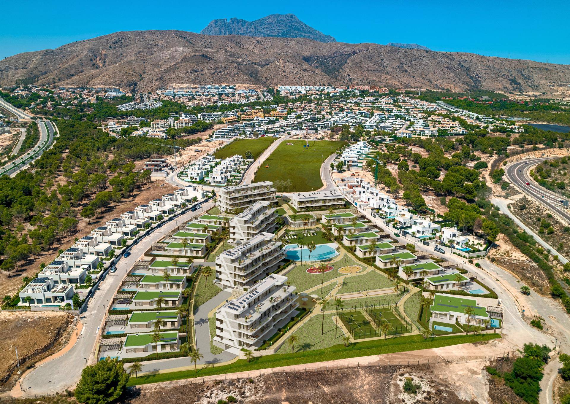 Weitläufige Wohnanlage mit modernen Gebäuden, Pools und Tennisplätzen in einer bergigen Landschaft.