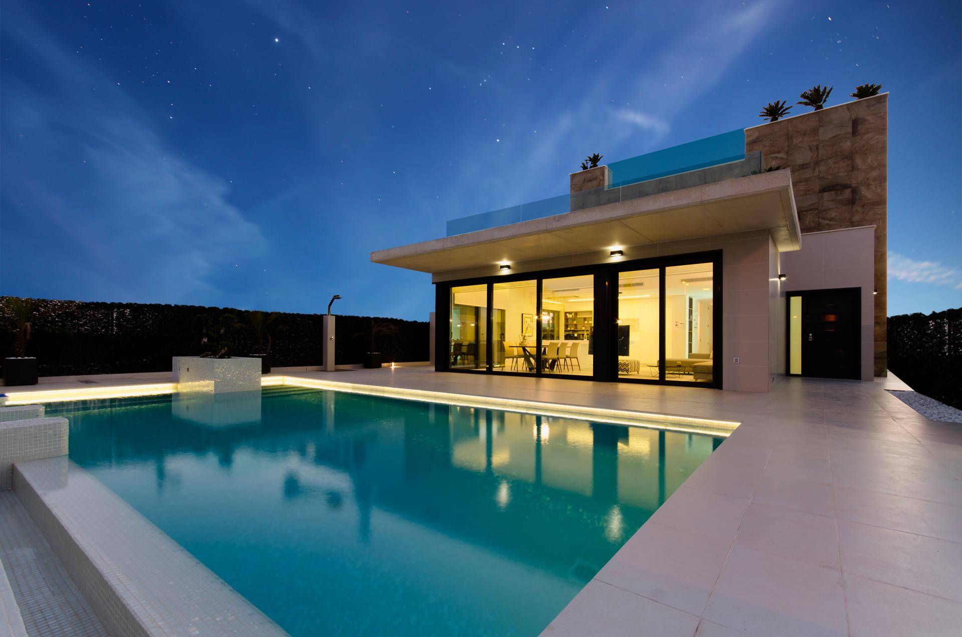 Elegante Villa mit beleuchtetem Poolbereich und moderner Architektur in der Abenddämmerung.