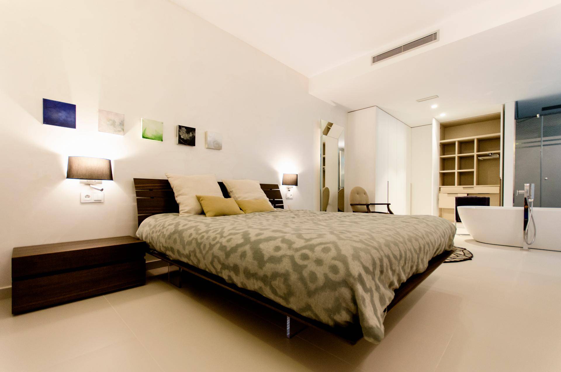 Modernes Schlafzimmer mit großem Bett, offenem Kleiderschrank und freistehender Badewanne.