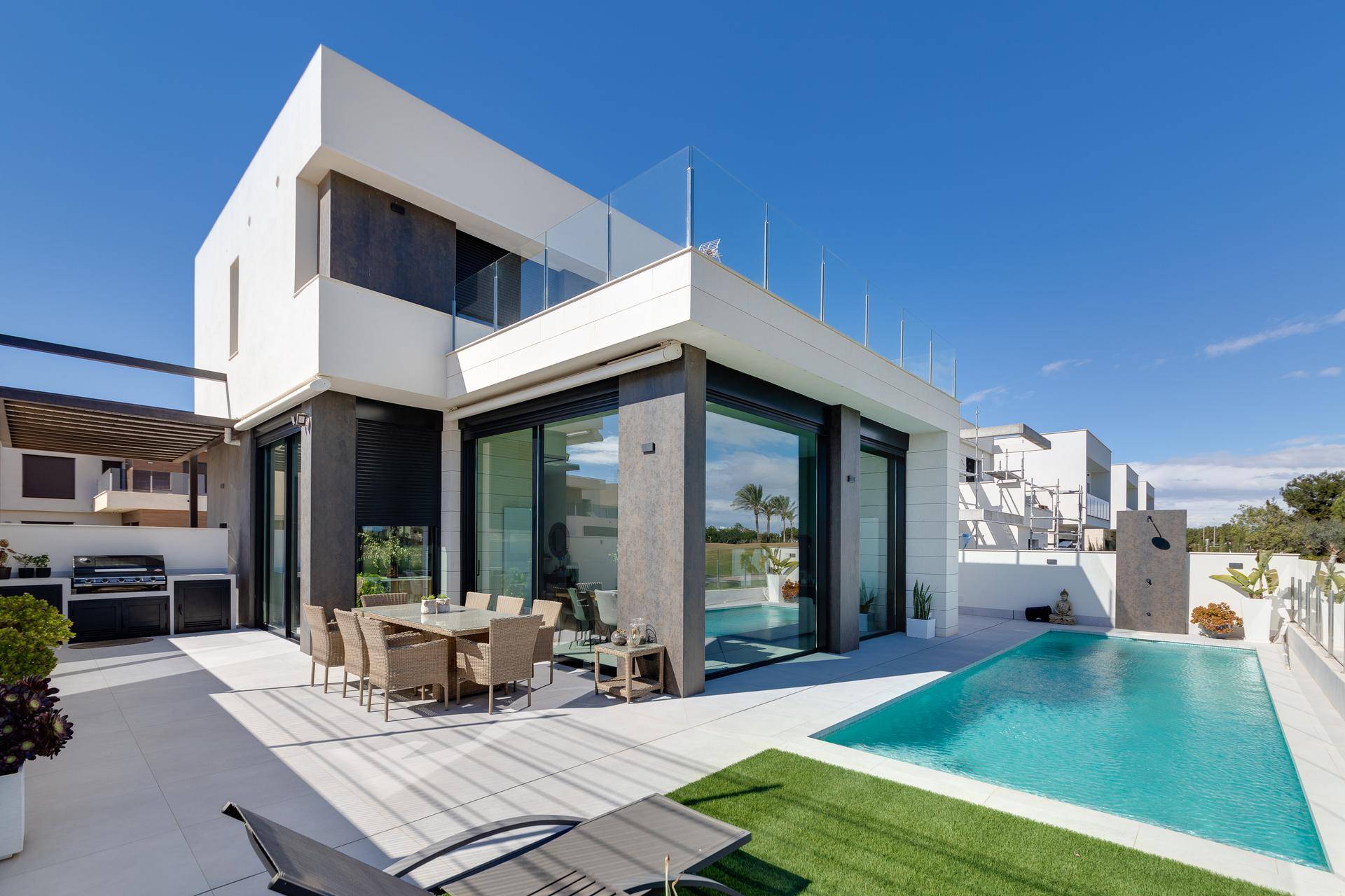Moderne Villa mit privatem Pool, großer Terrasse und Essbereich im Freien unter blauem Himmel.