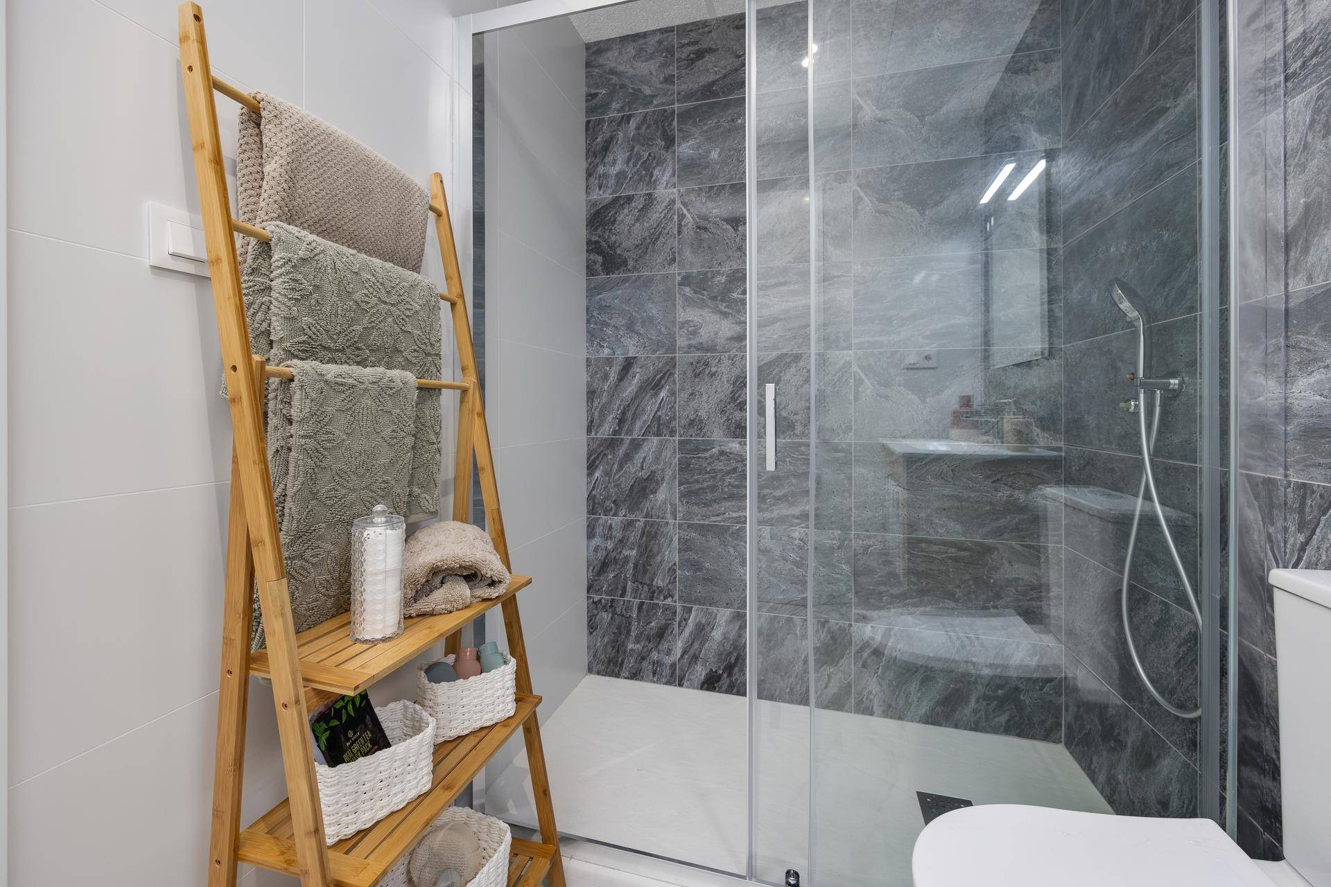 Modernes Badezimmer mit begehbarer Dusche, grauen Marmorfliesen und Holzleiter als Handtuchhalter.