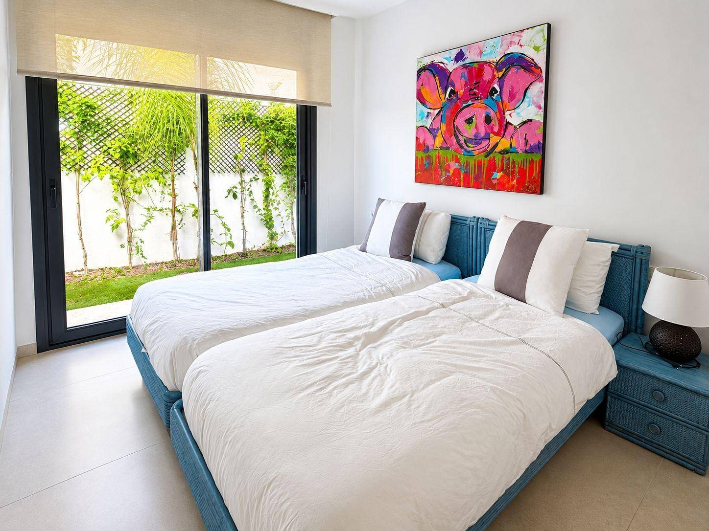 Helles Schlafzimmer mit zwei Einzelbetten, farbenfroher Kunst und Blick ins Grüne.