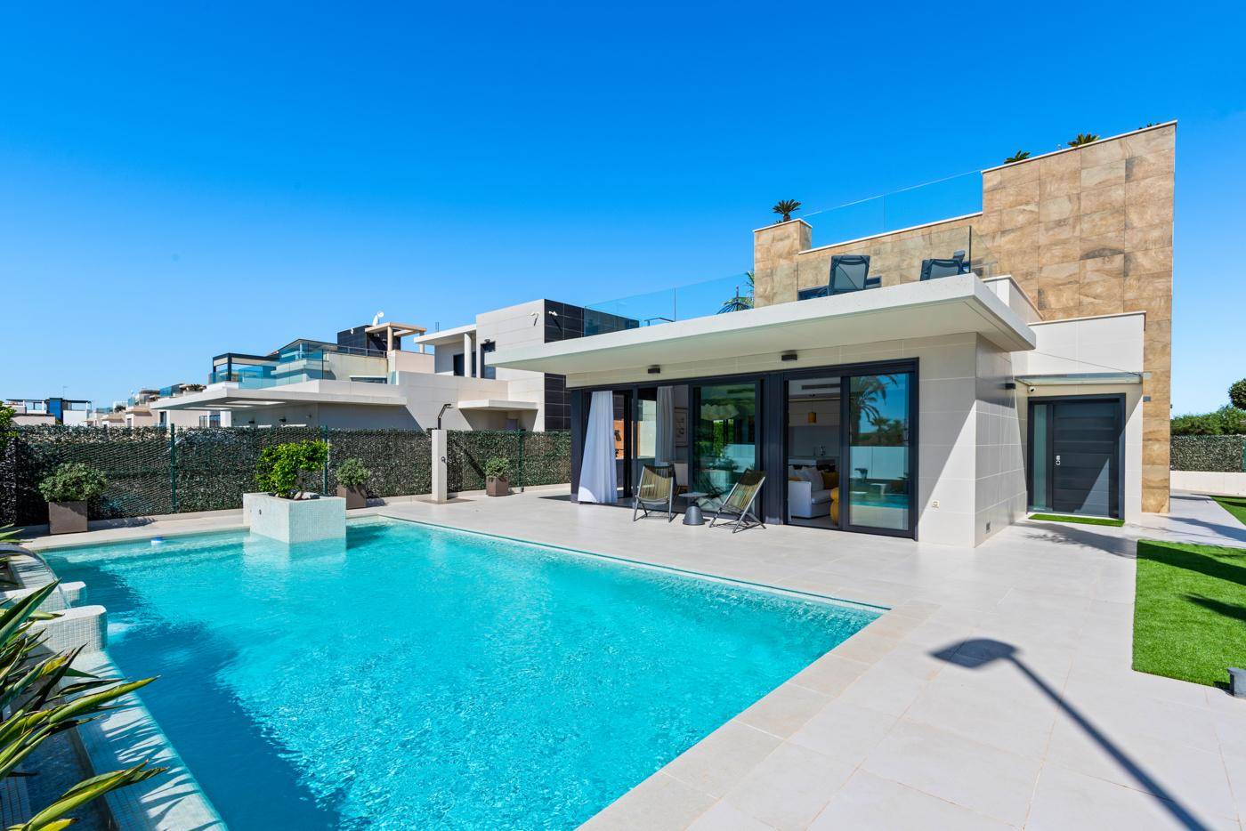 Elegante Villa mit weitläufigem Poolbereich, Liegestühlen und moderner Architektur unter strahlendem Himmel.