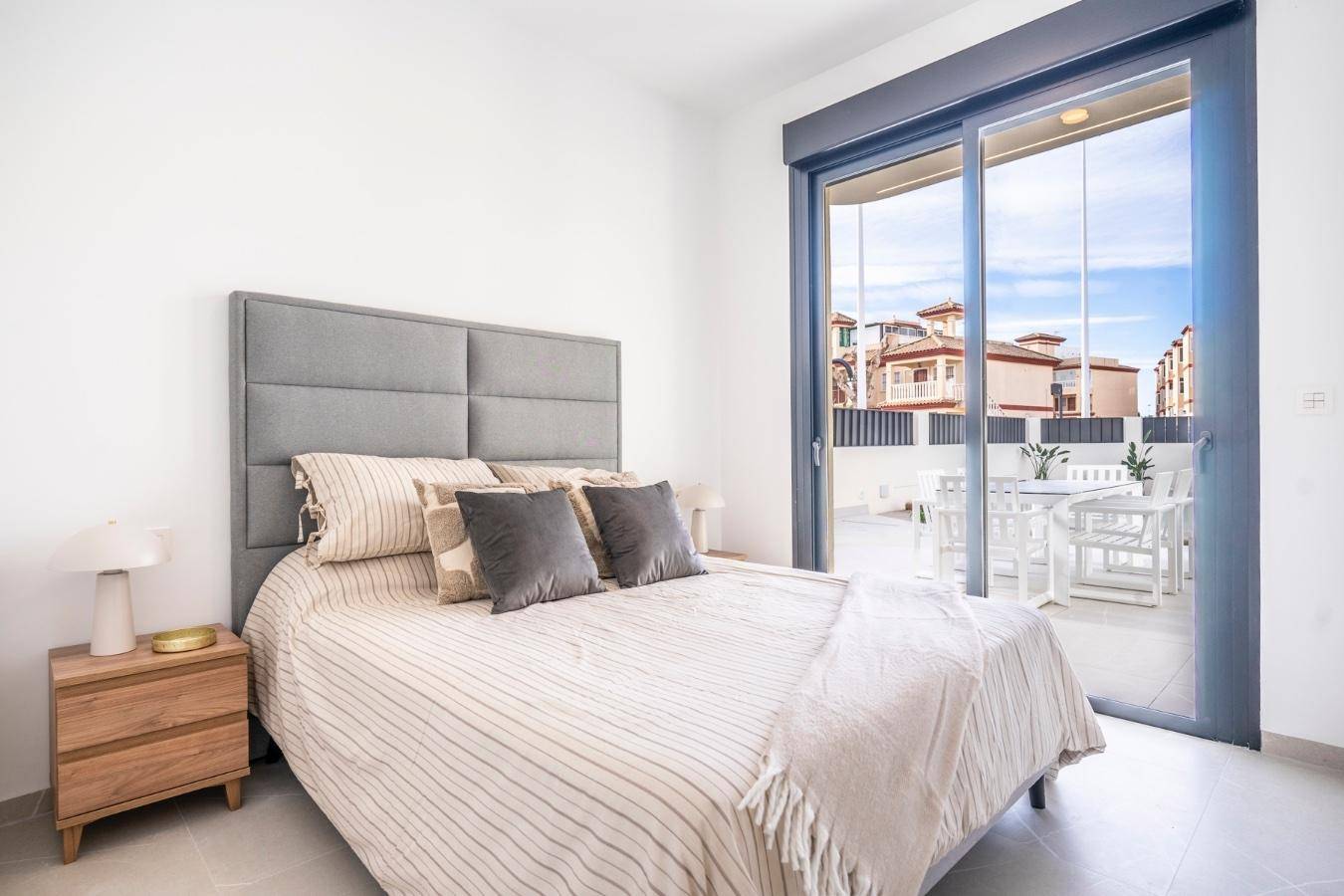 Helles Schlafzimmer mit Doppelbett und großem Schiebefenster, das Zugang zu einer Terrasse bietet.