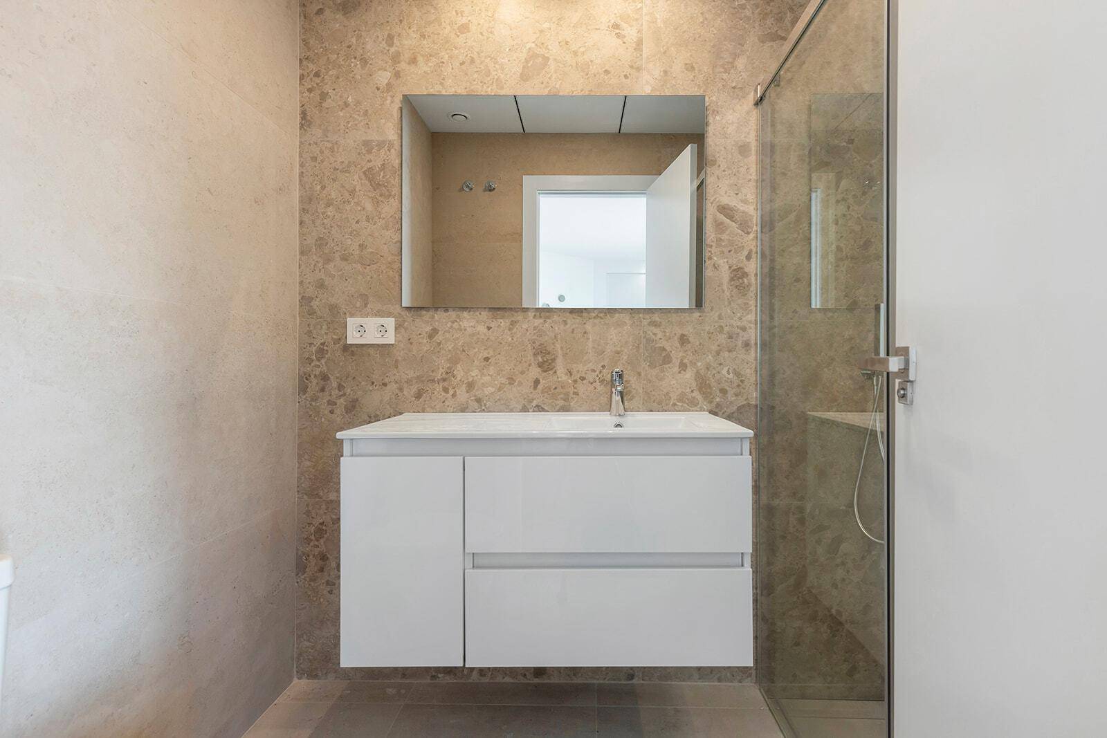 Modernes Badezimmer mit braunen Marmorfliesen, großem Spiegel und schwebendem Waschtisch.
