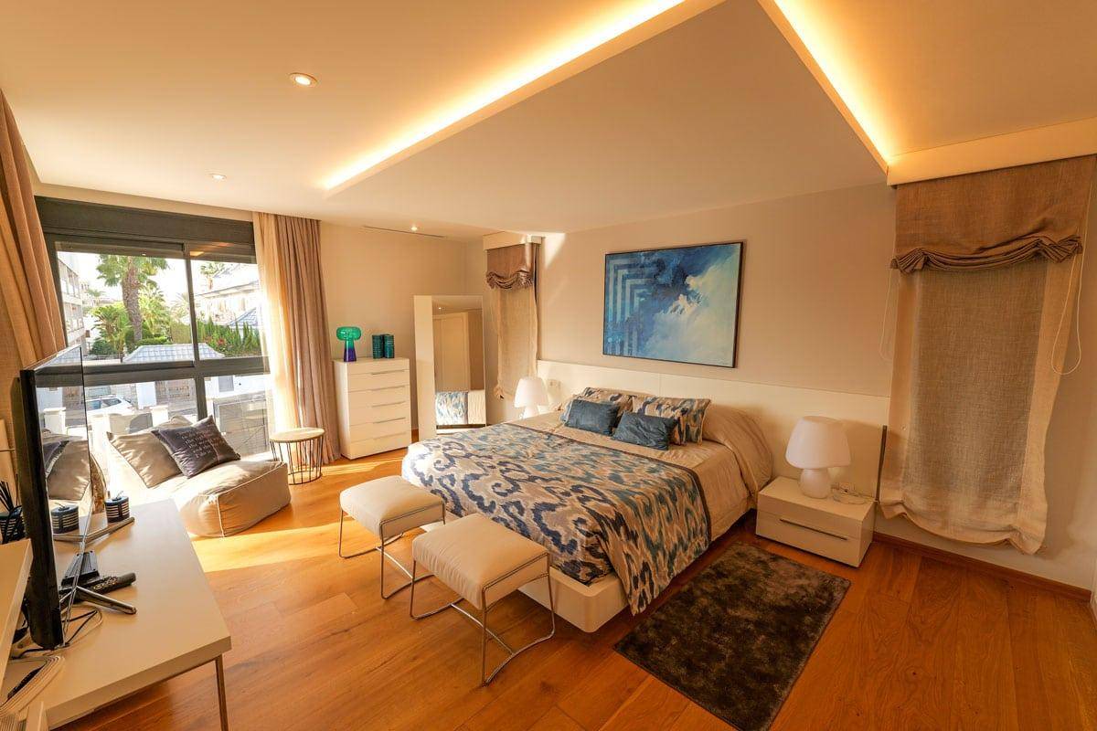 Gemütliches Schlafzimmer mit Holzboden, großem Fenster und indirekter Deckenbeleuchtung.