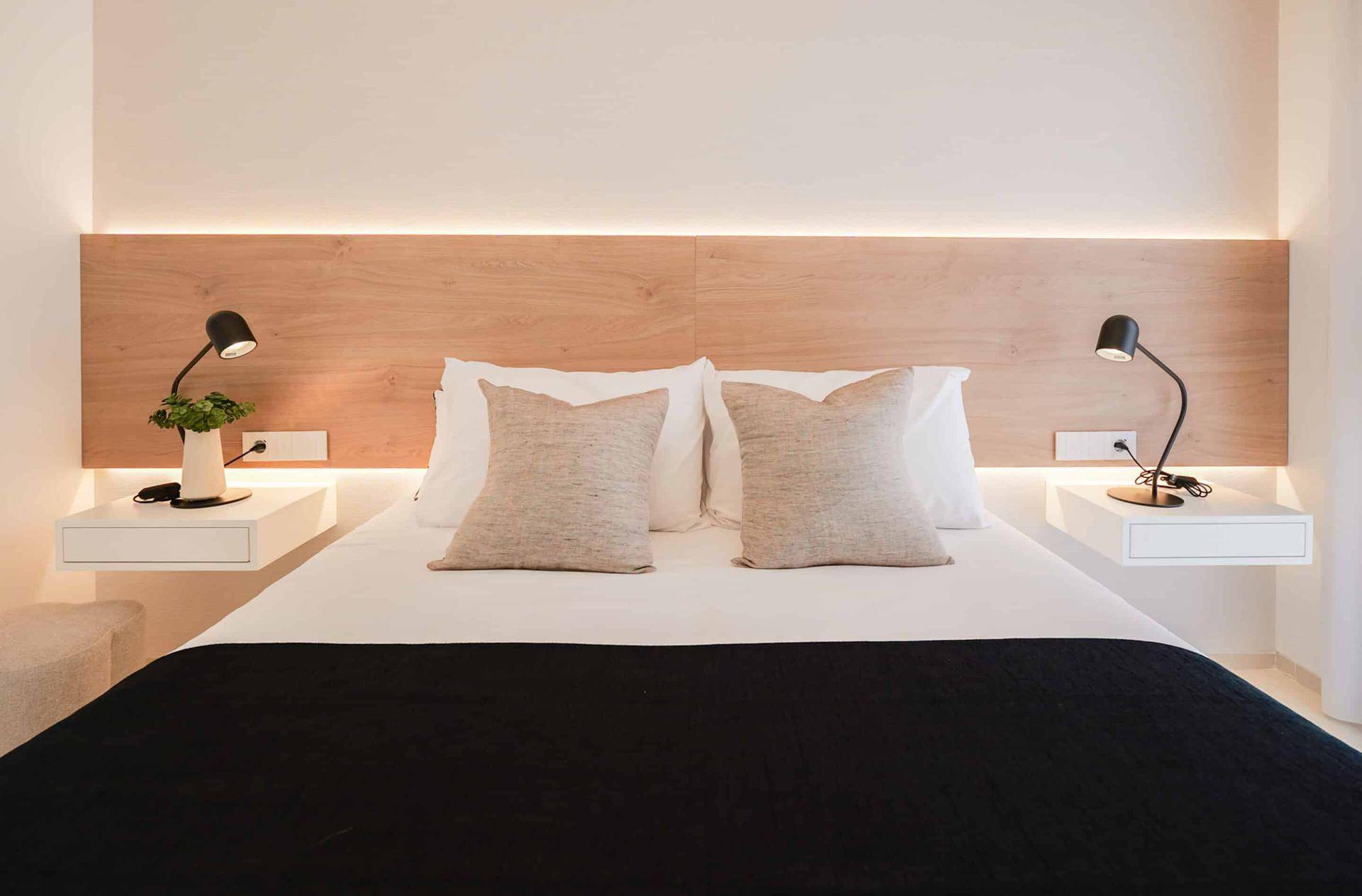 Helles Schlafzimmer mit Holz-Kopfteil, indirekter Beleuchtung und schwebenden Nachttischen.