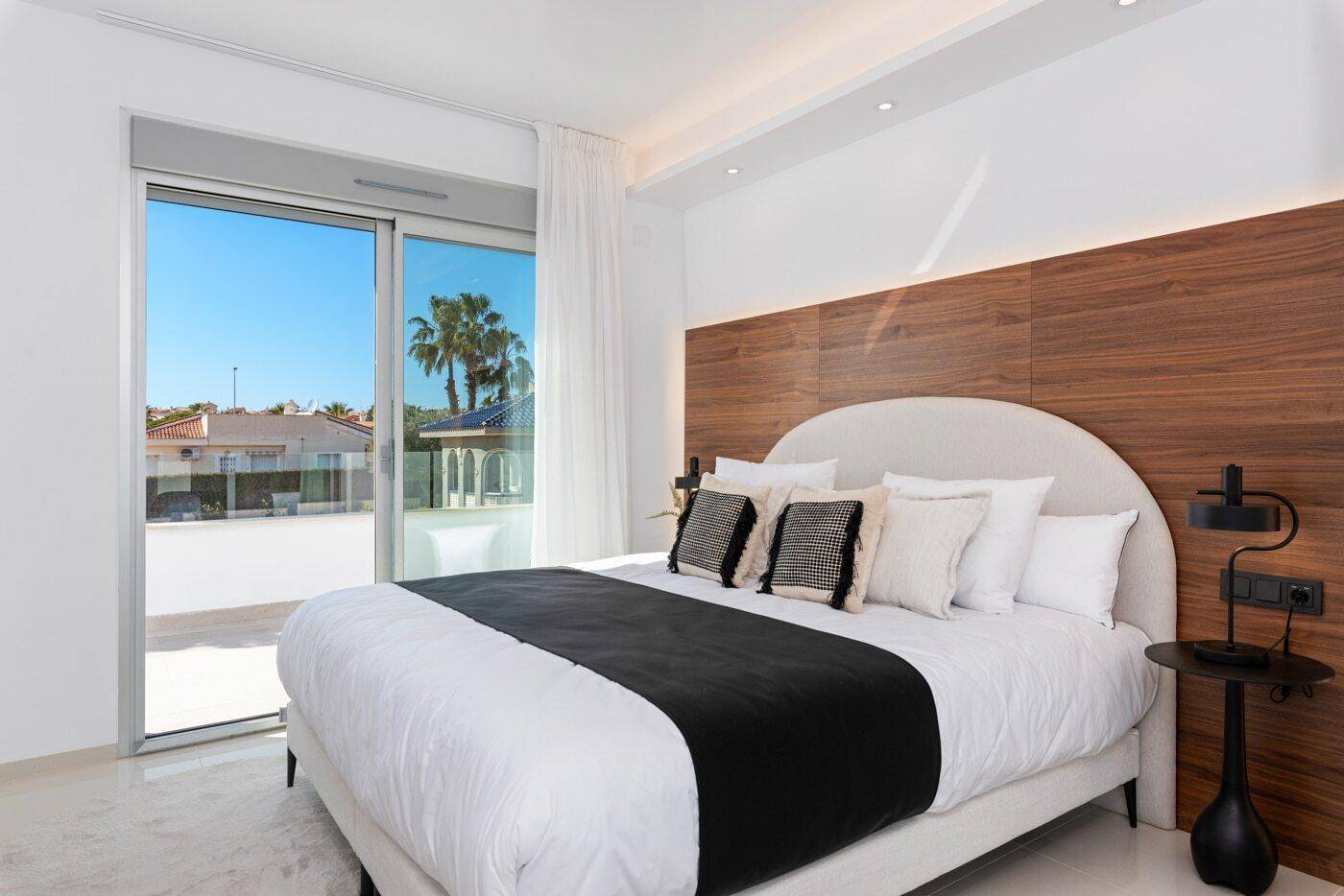 Elegantes Schlafzimmer mit großem Bett, Holzakzentwand und Zugang zum Außenbereich.