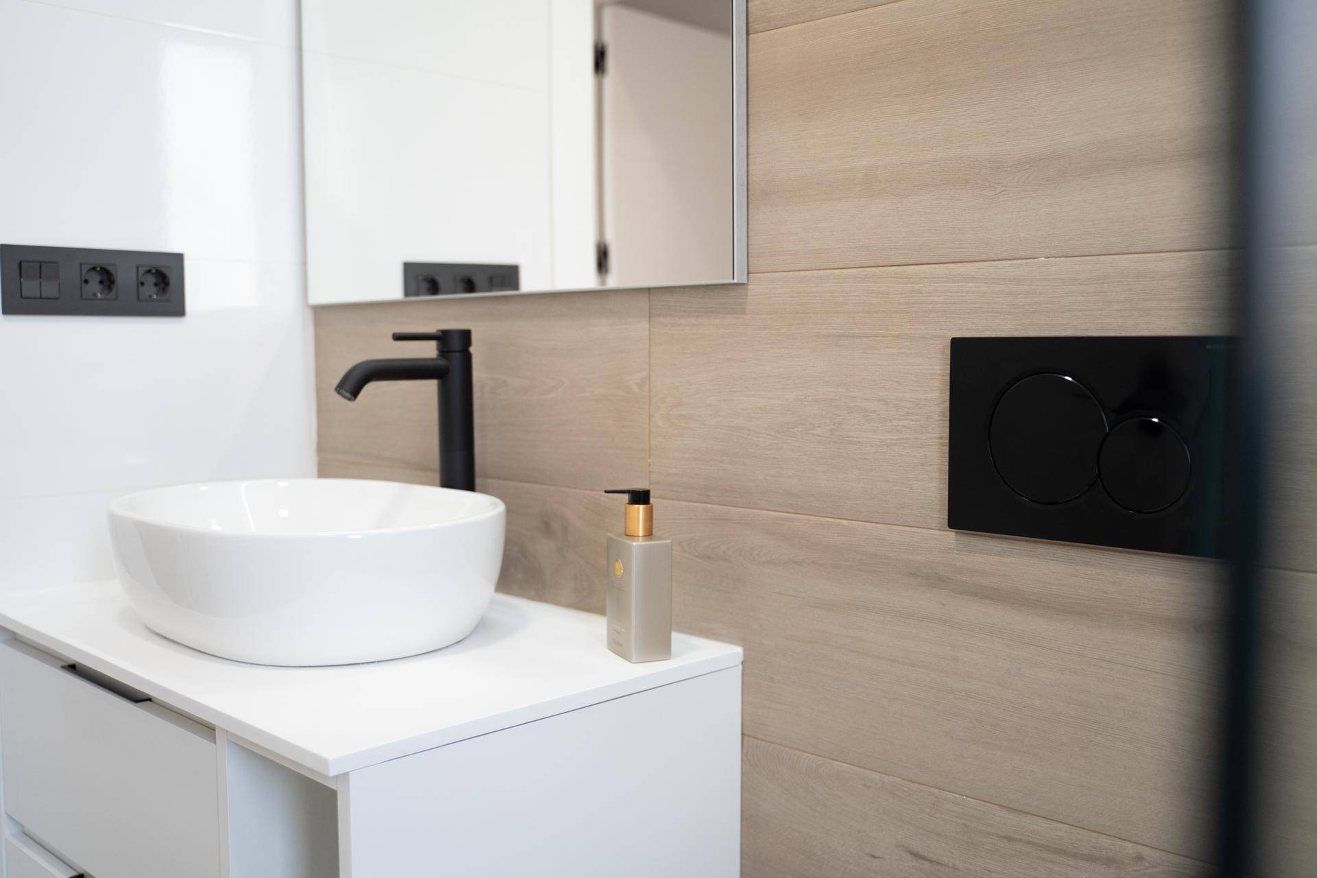 Modernes Badezimmer mit Aufsatzwaschbecken, Holzoptikfliesen und schwarzen Armaturen.
