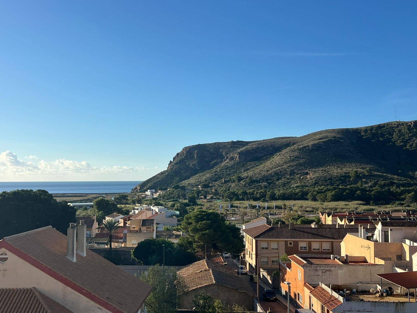 Weitläufiger Blick über die Dächer einer Küstenstadt auf das Meer und die grünen Berge.