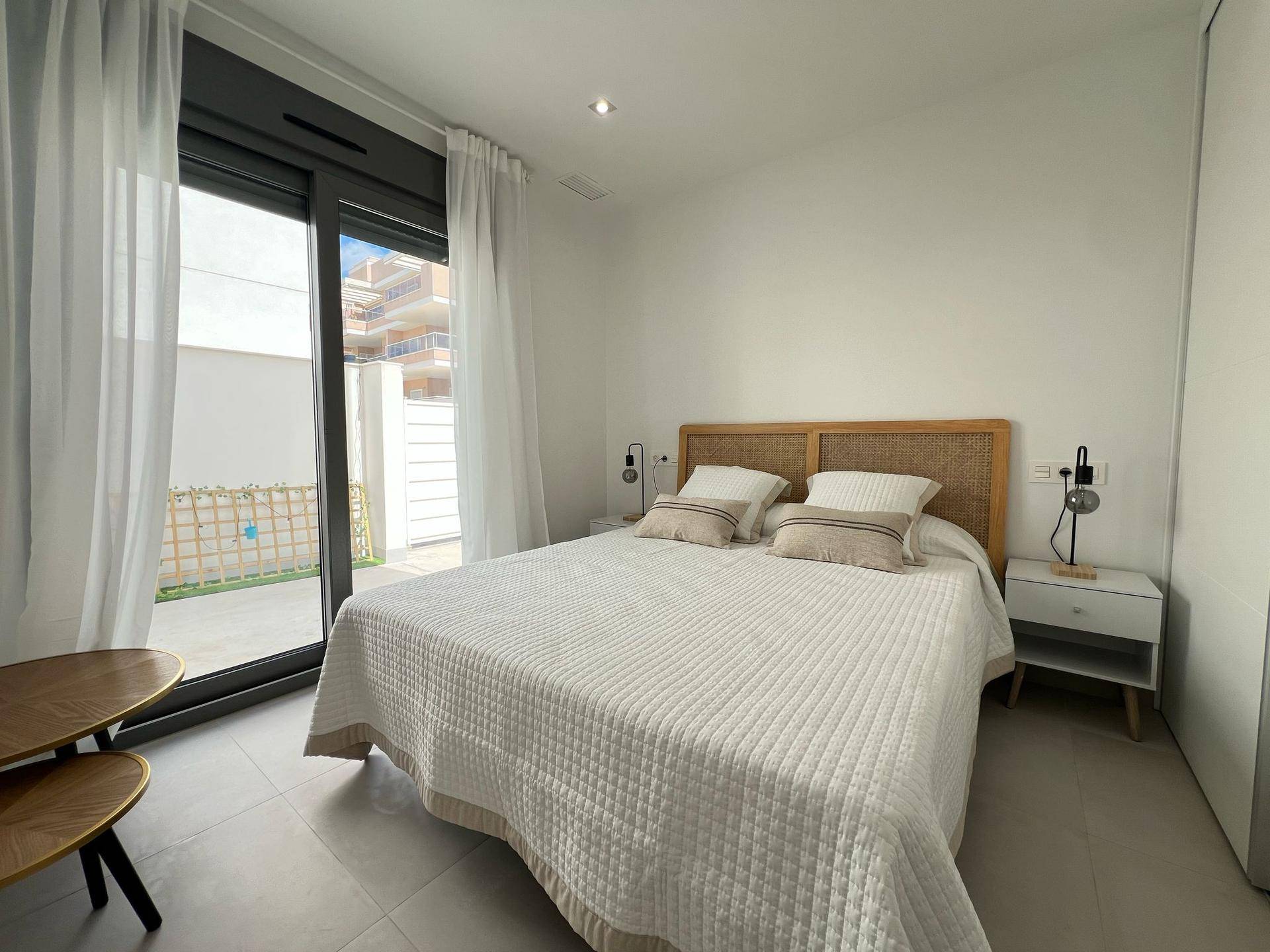 Schlafzimmer mit Doppelbett, Nachttischen und großem Fenster mit Zugang zum Außenbereich.