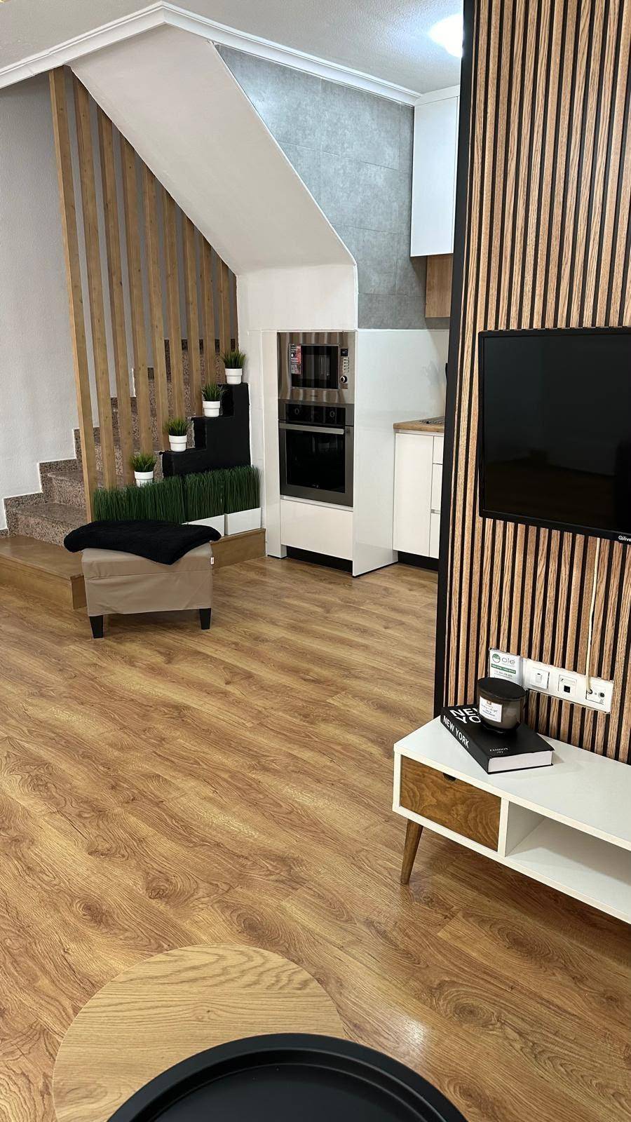 Offener Wohnbereich mit moderner Holzlamellenwand, Treppe und integrierter Küche im Hintergrund.