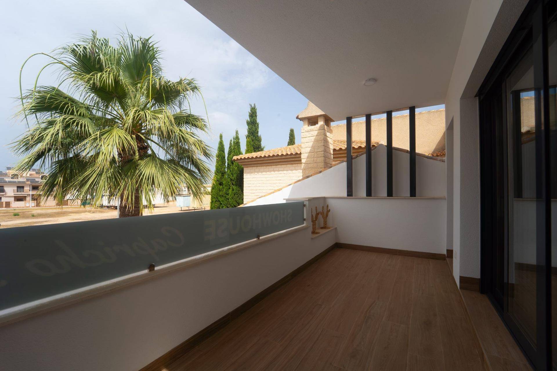 Heller Balkon mit Glasgeländer und Blick auf Palmen, umliegende Gebäude und die Landschaft.