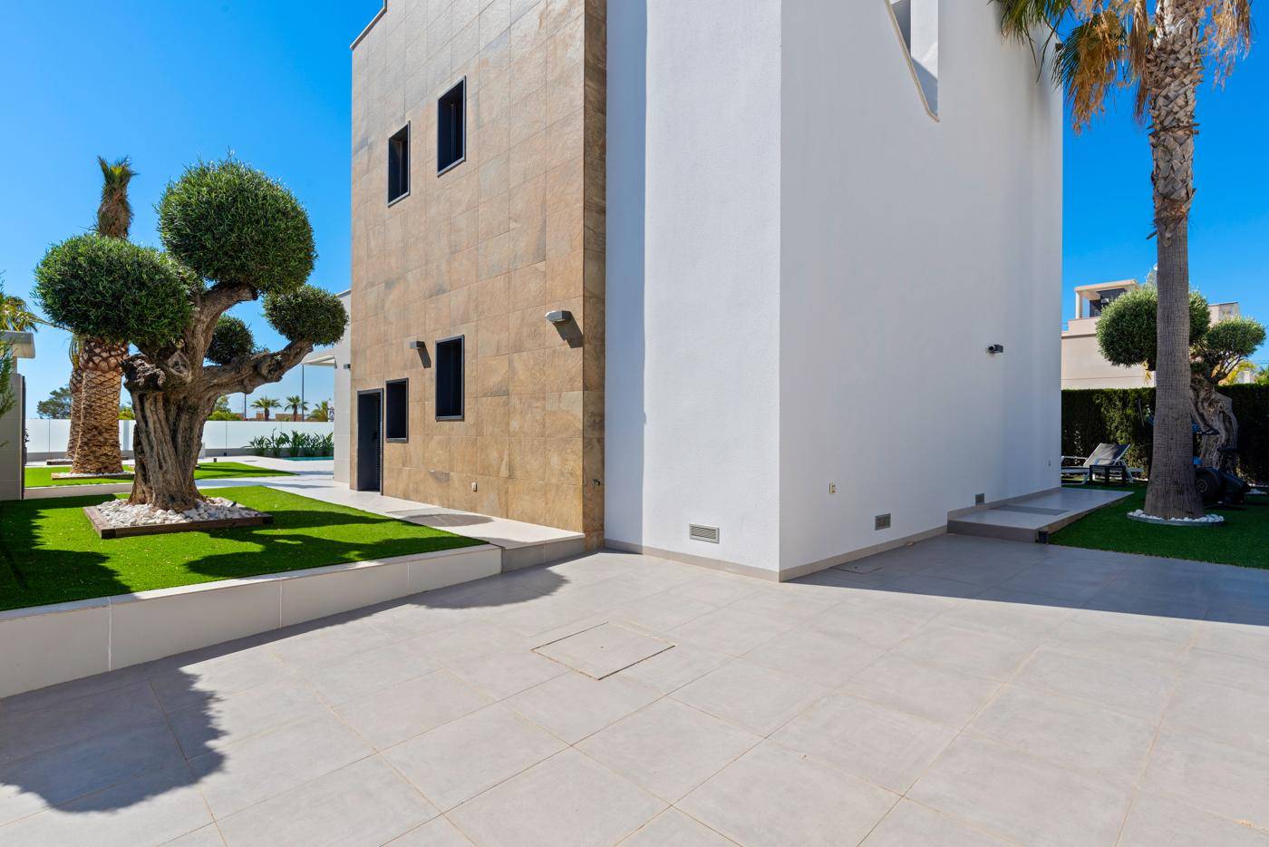 Moderne Hausfassade mit heller Verkleidung und gepflastertem Bereich unter blauem Himmel.
