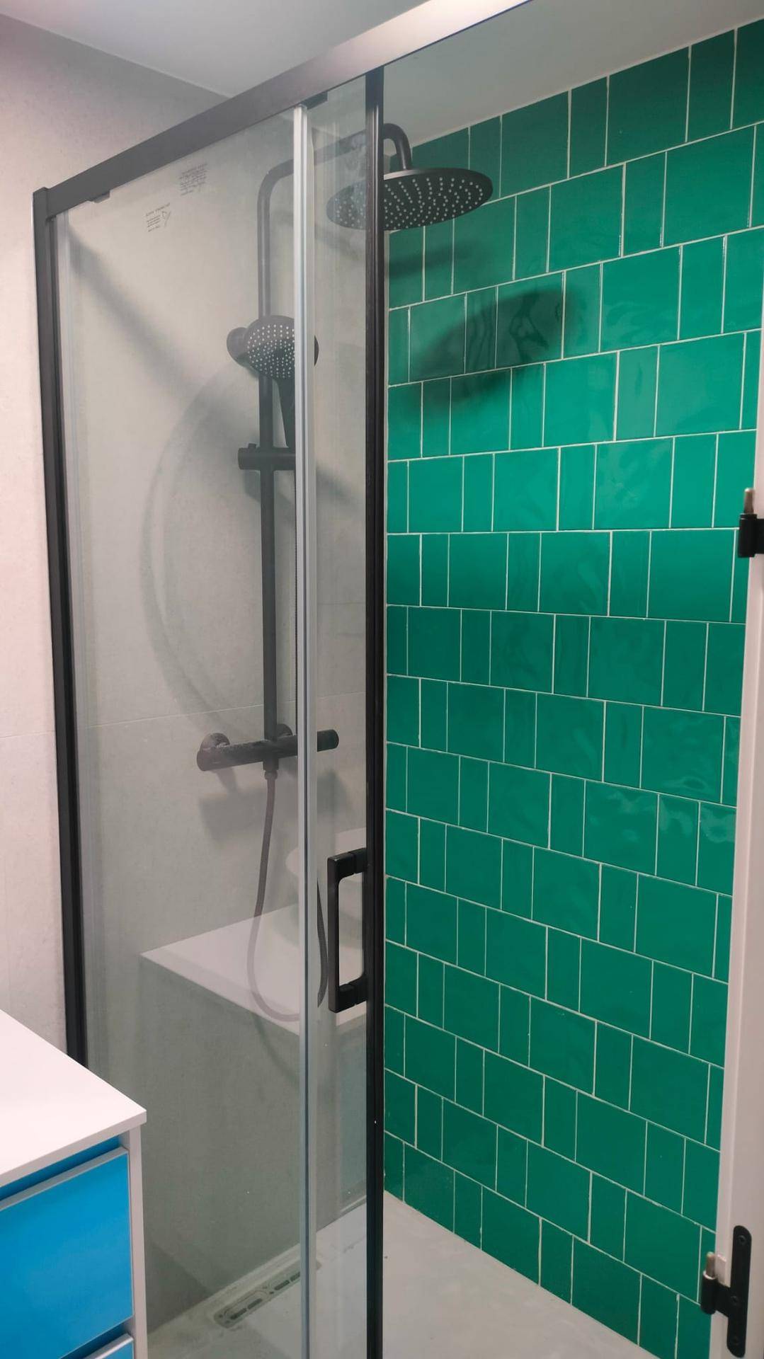 Ebenerdige Dusche mit grünen Wandfliesen und schwarzen Armaturen im modernen Bad.