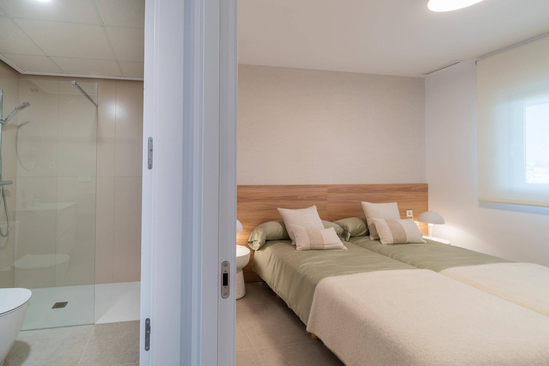 Schlafzimmer mit zwei Einzelbetten und Blick auf das angrenzende Badezimmer mit Dusche.