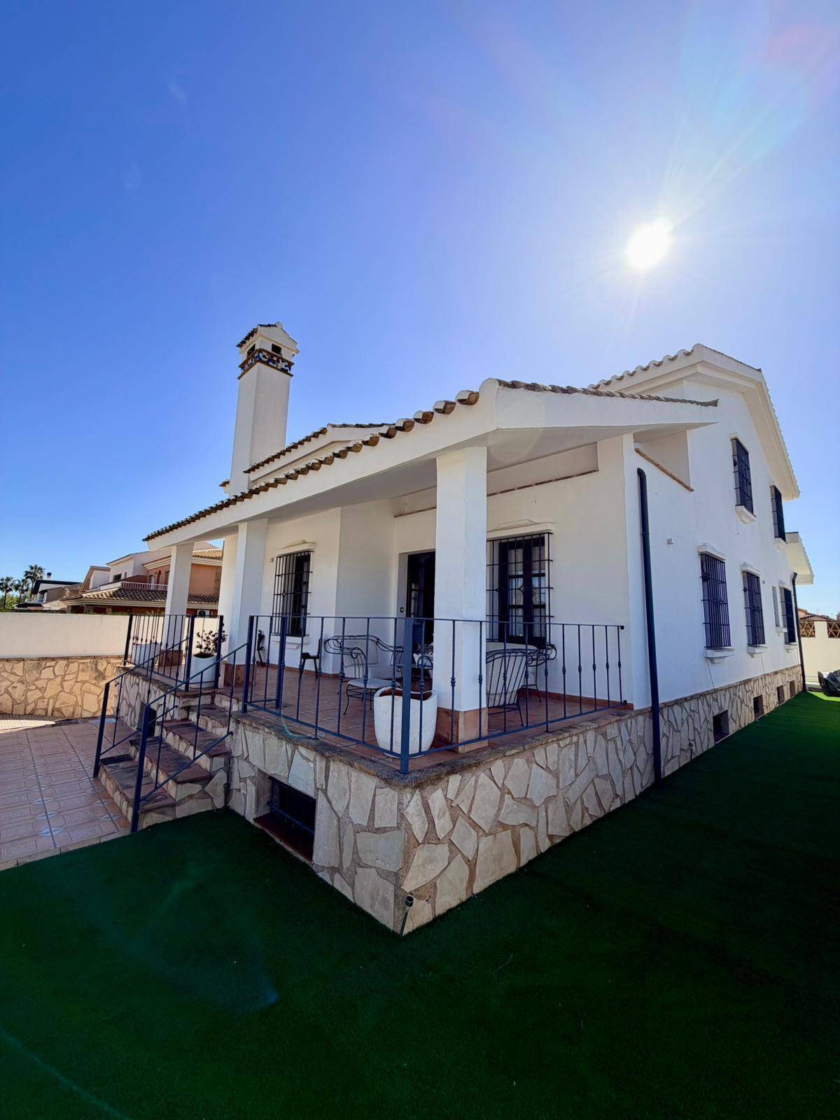 Seitenansicht der Villa mit Kunstrasenfläche, Steinfassade und überdachter Terrasse.