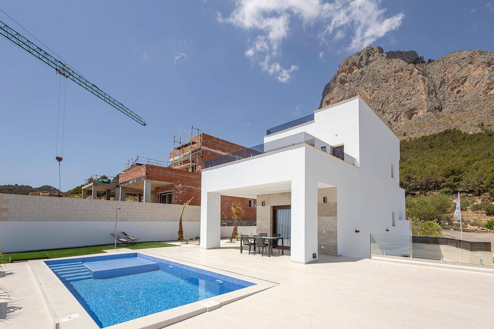 Moderne Villa mit Pool und Terrasse, umgeben von einer Baustelle und Bergen.