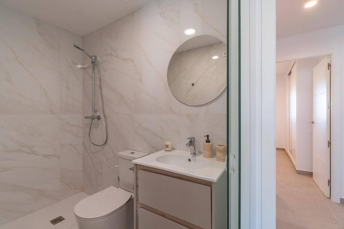 Elegantes Badezimmer mit Marmoroptik-Fliesen, ebenerdiger Dusche, WC und Waschtisch.