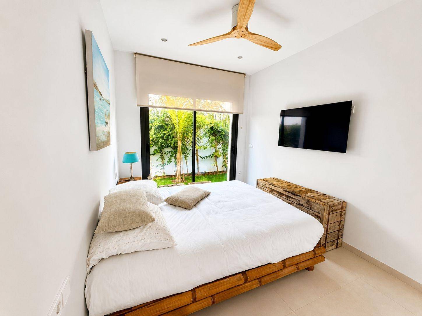Helles Schlafzimmer mit Bambusbett, Deckenventilator und großen Fenstern zum Garten.