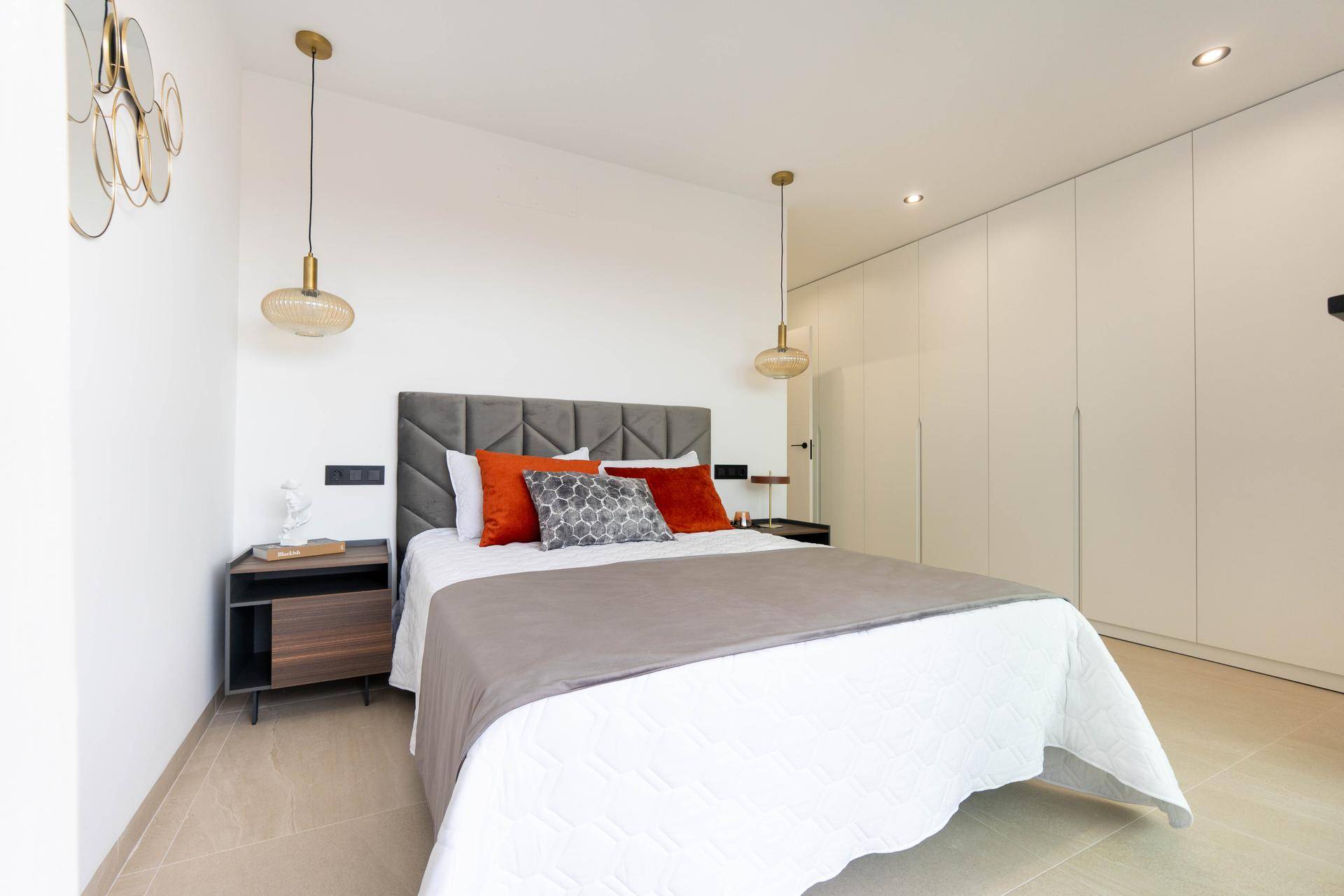 Elegantes Schlafzimmer mit Einbauschränken, modernem Bett und dekorativen Hängelampen.