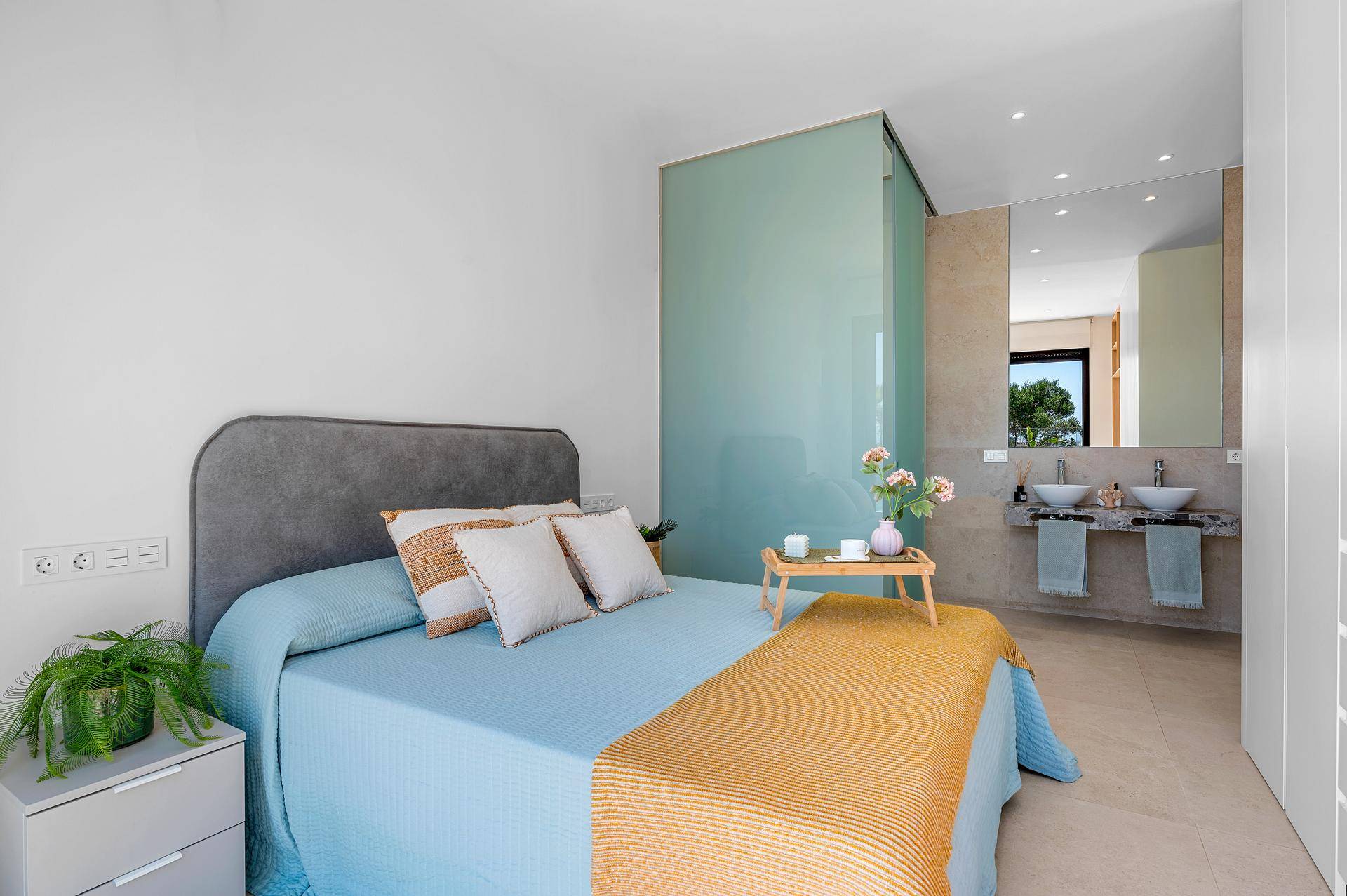 Schlafzimmer mit integriertem Badbereich, abgetrennt durch eine Milchglaswand, mit Doppelwaschbecken.