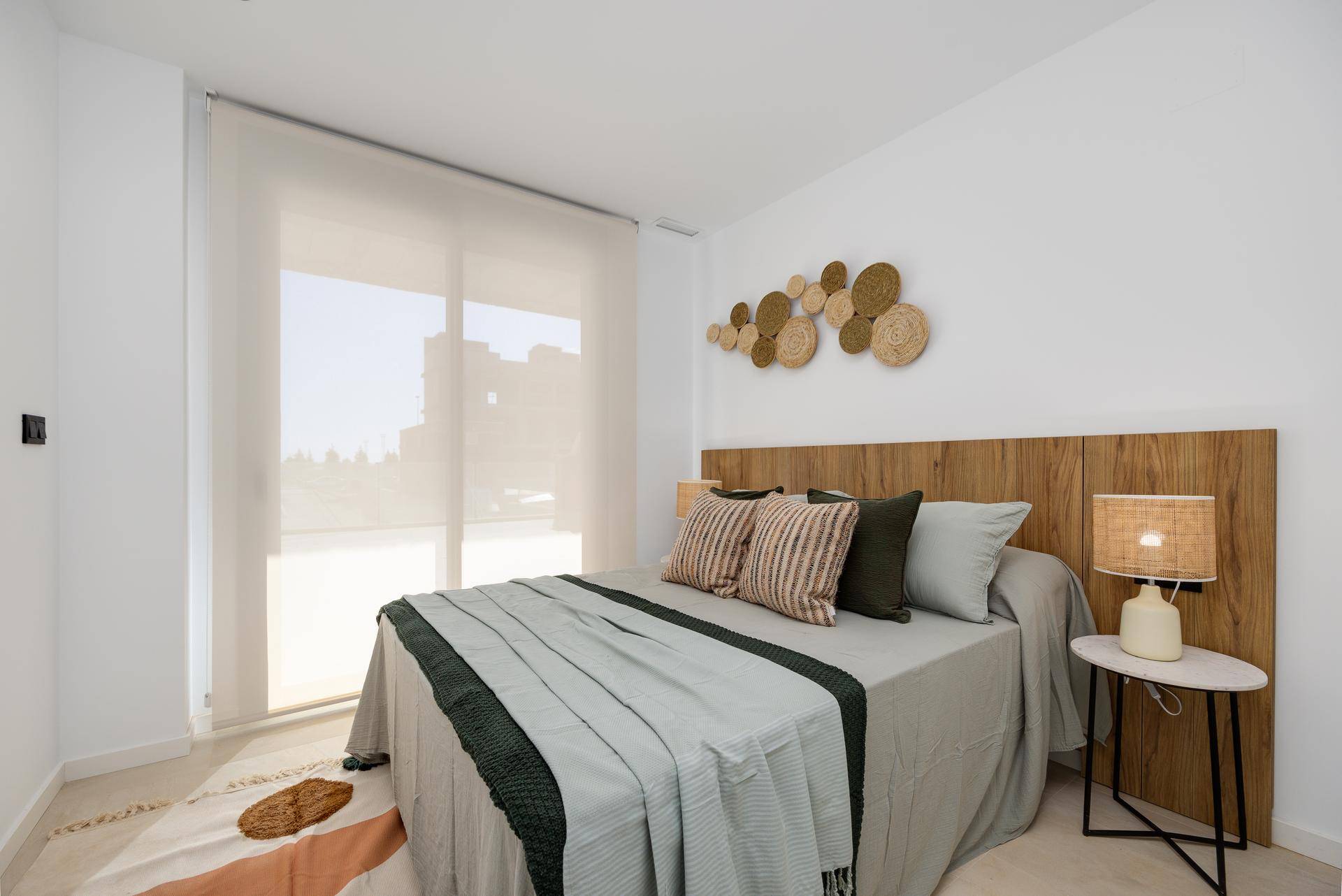 Helles Schlafzimmer mit modernem Bett, Holz-Kopfteil und großem Fenster für natürliche Beleuchtung.