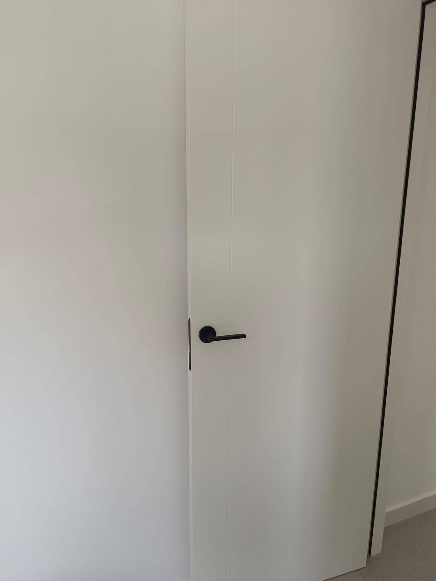 Weiße Innentür mit schwarzem Griff in einem minimalistisch gestalteten Flur.