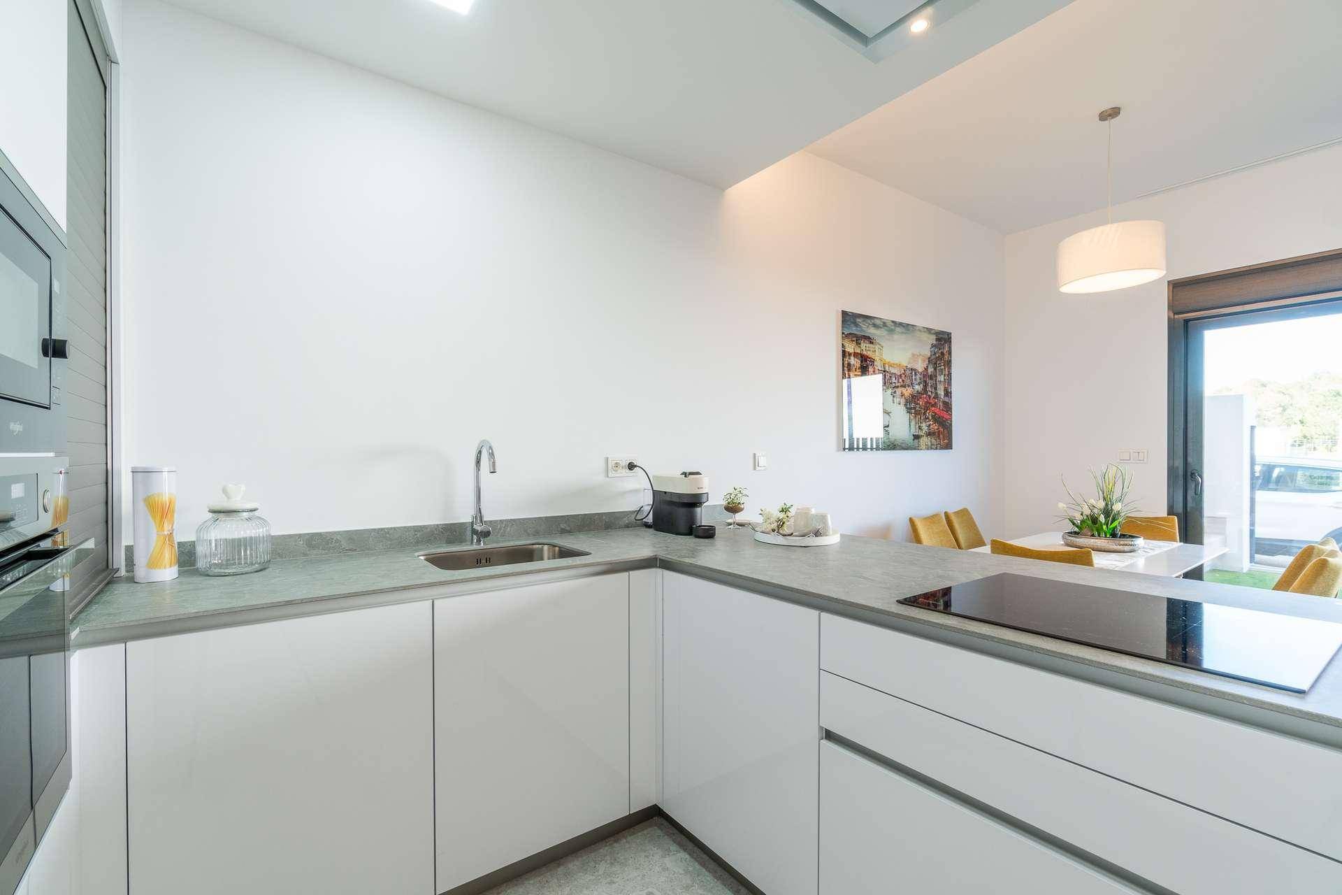 Moderne Einbauküche mit weißen Fronten, Induktionskochfeld und Essbereich im Hintergrund.
