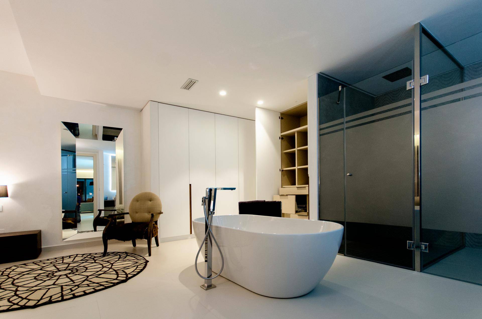 Luxuriöses Schlafzimmer mit freistehender Badewanne, Glasdusche und offenem Kleiderschrank.